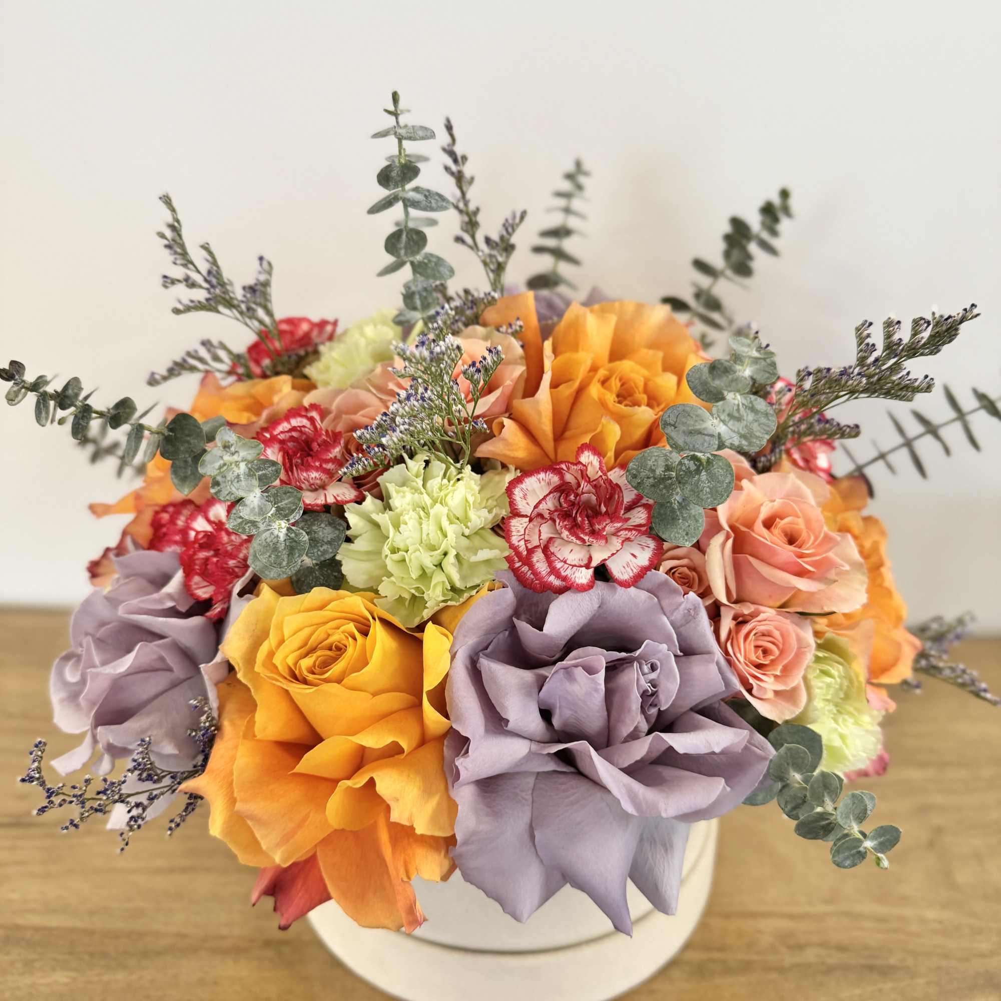 Bouquet of orange, lavender, and peach roses with carnations in a white box