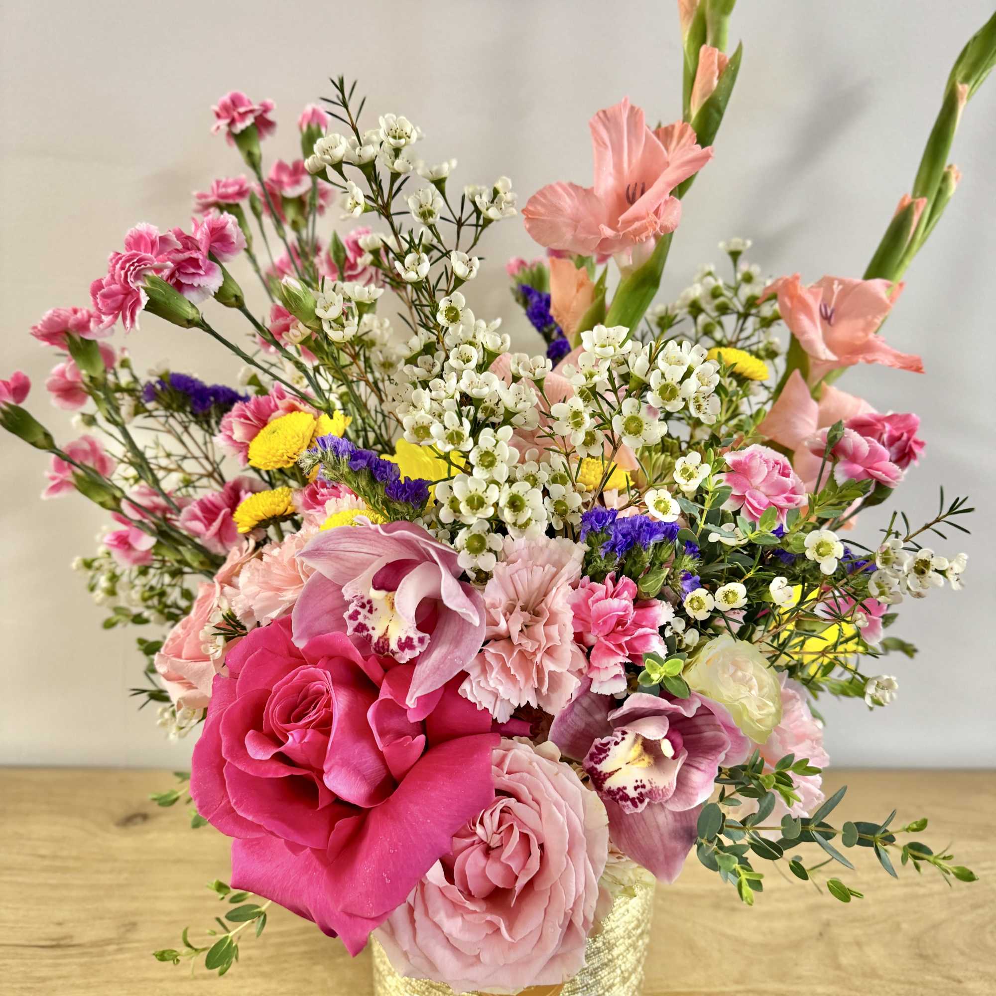 Colorful arrangement of pink roses, carnations and mixed blooms in a gold textured vase
