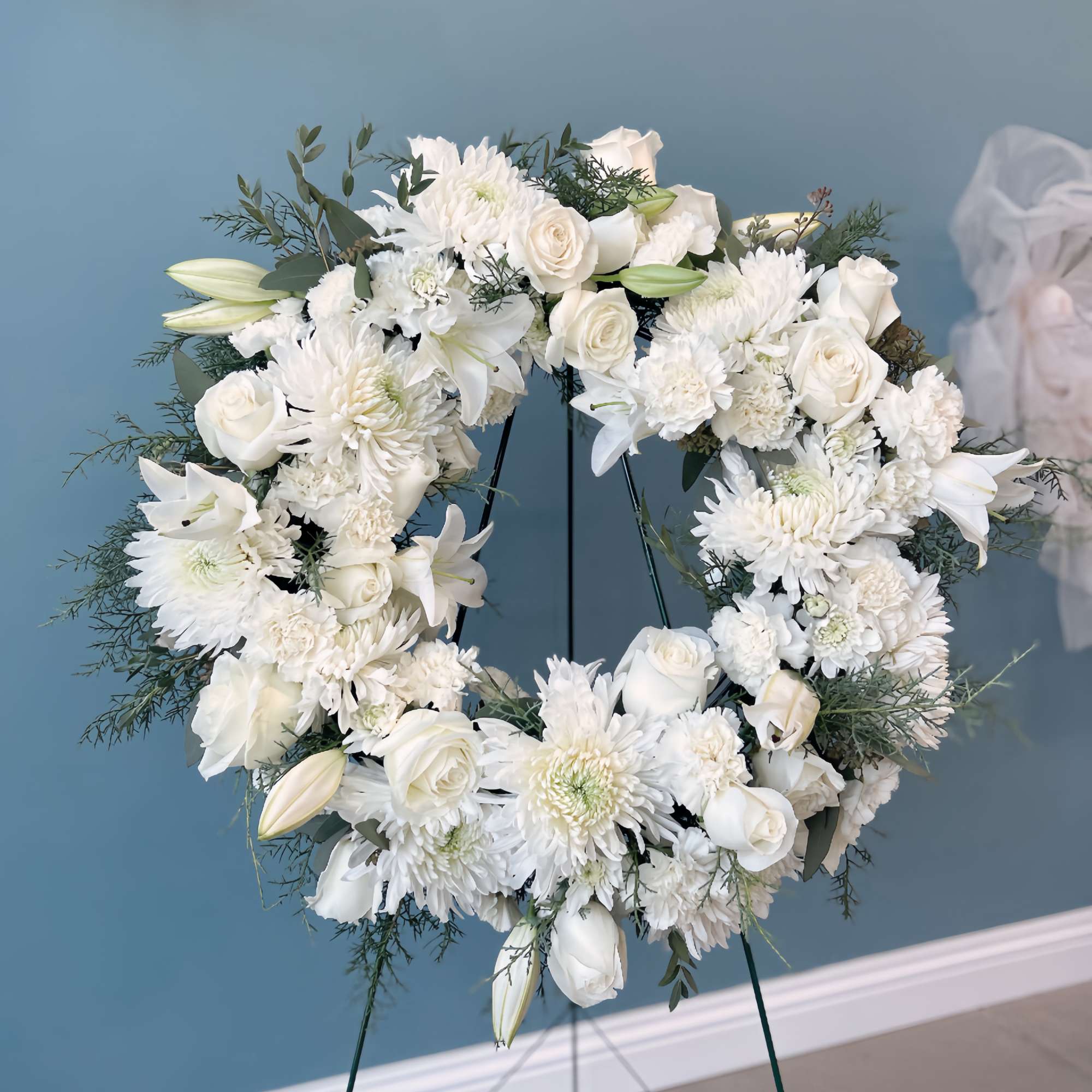 White floral wreath on a stand with roses, lilies, and chrysanthemums