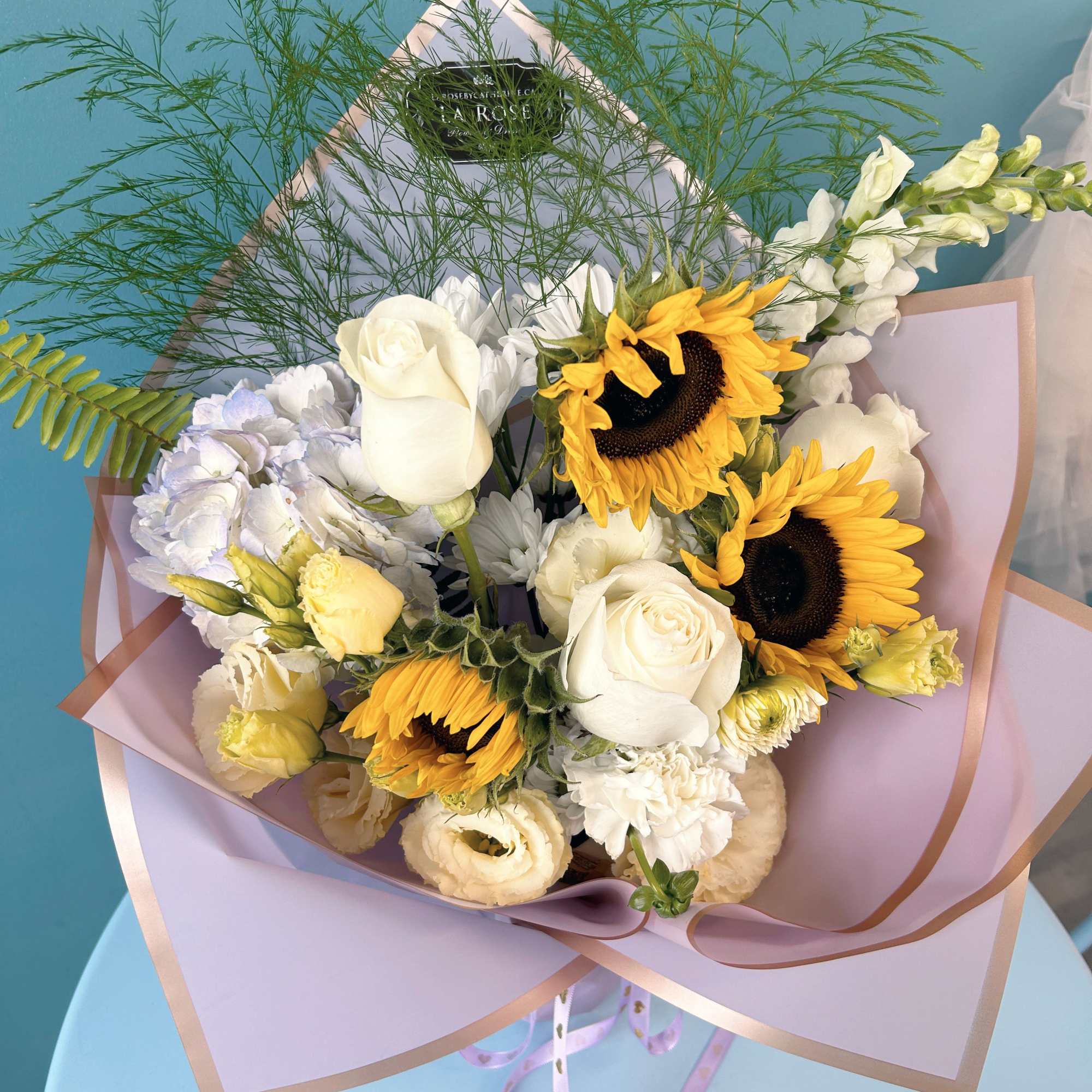 Bouquet of white roses, sunflowers, and pale blooms wrapped in lavender paper