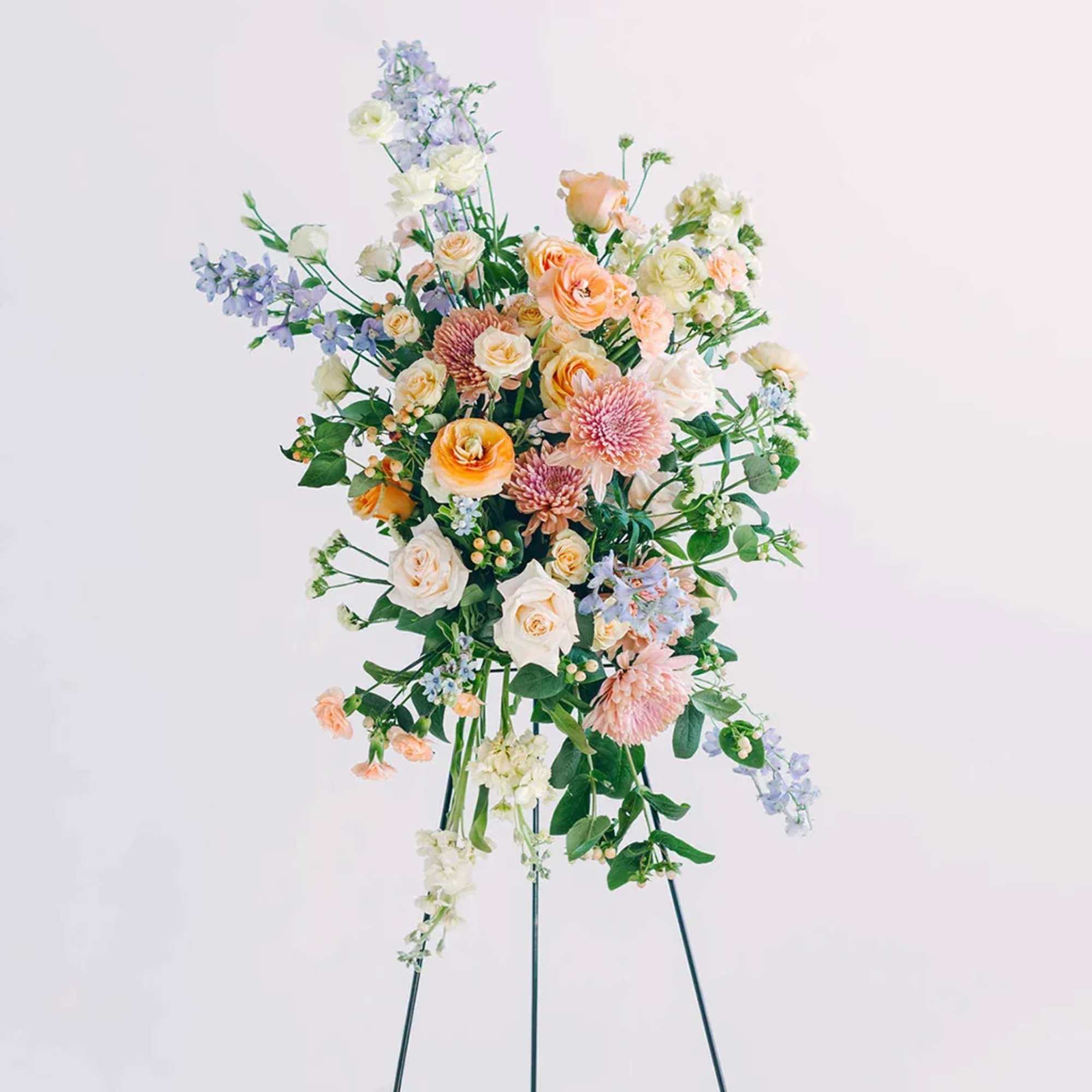 Tall pastel floral arrangement on a stand with peach, white, and lavender blooms
