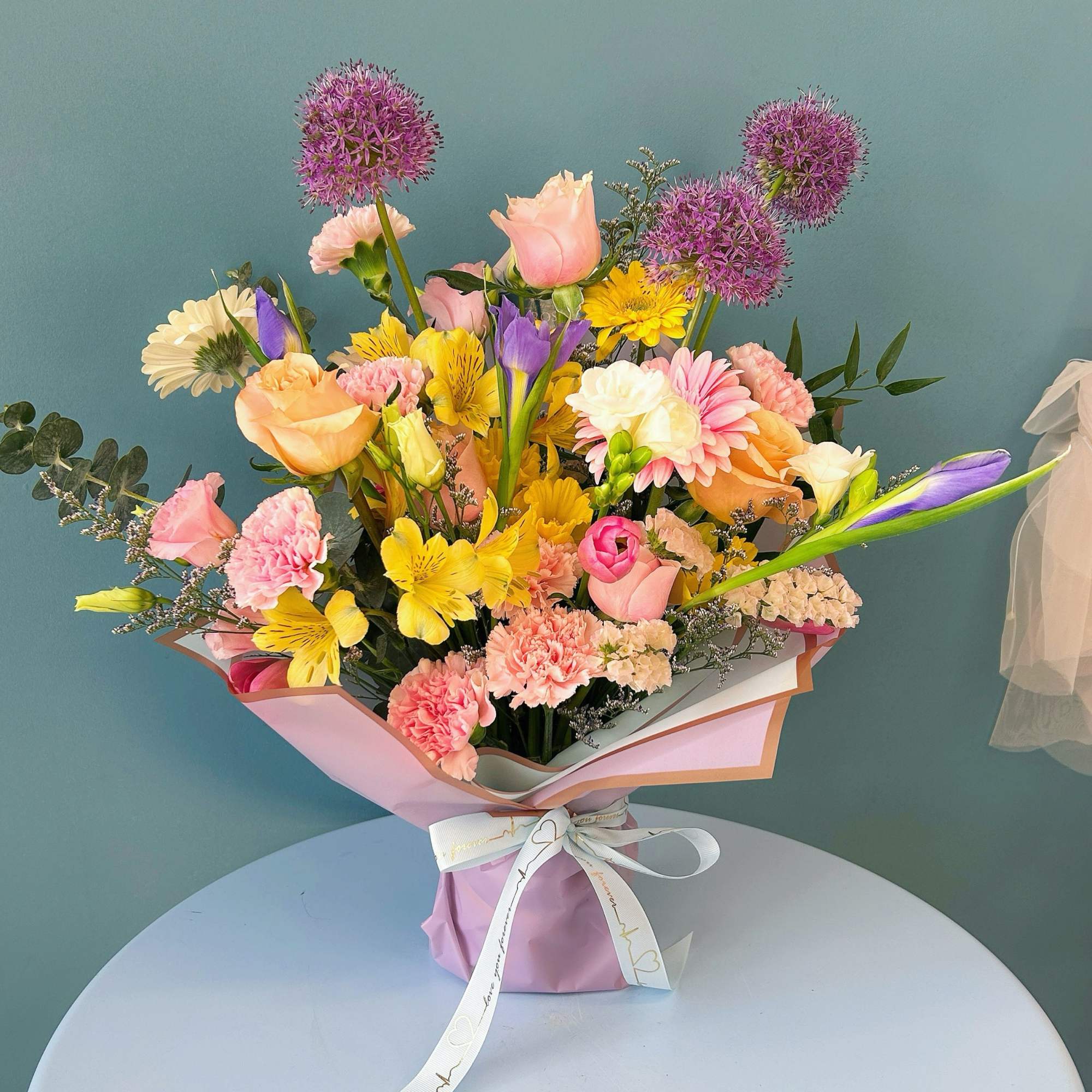 Mixed bouquet of pink, yellow, purple, and peach flowers in pastel wrapping