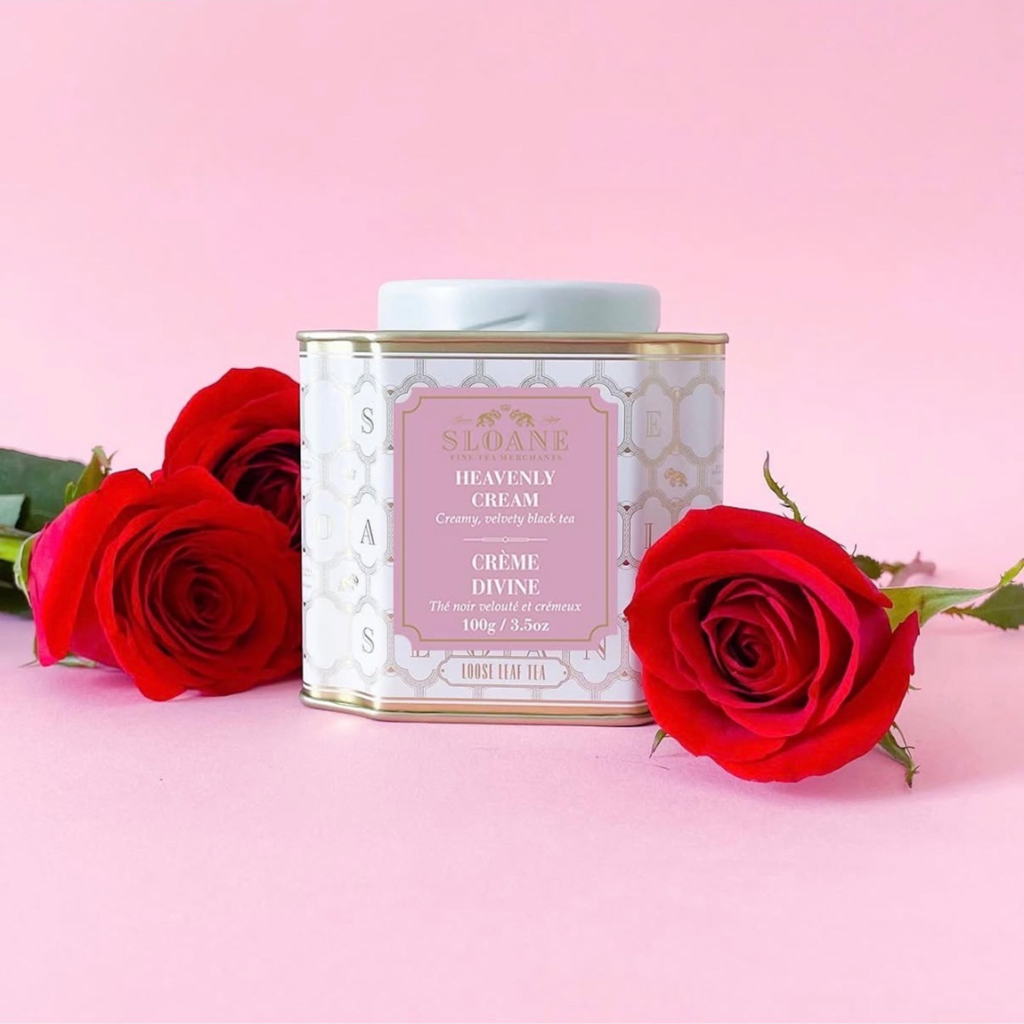 Red roses beside a decorative tea tin on a pink background