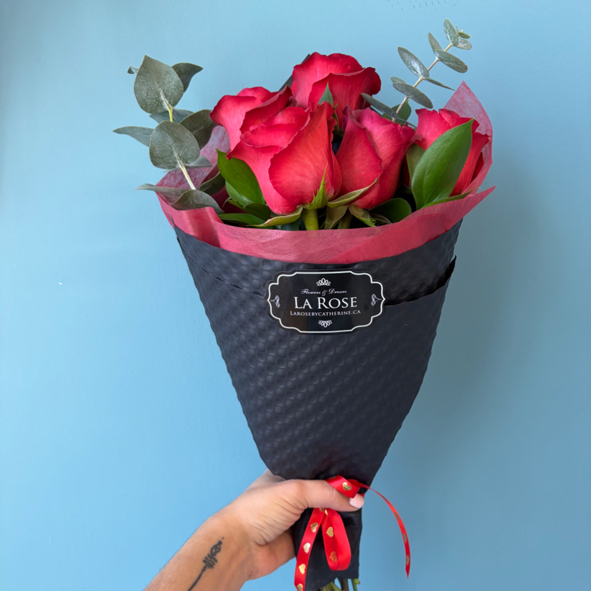 Handheld bouquet of red roses wrapped in black paper with a red ribbon