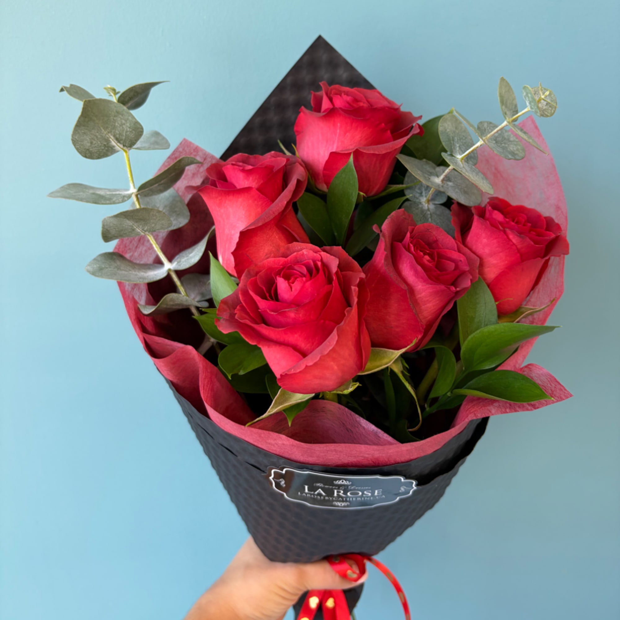 Handheld bouquet of red roses wrapped in black and pink paper