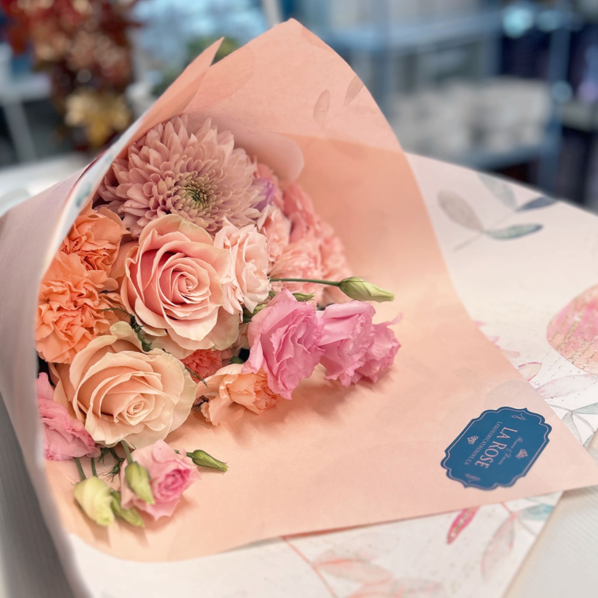 Pink and peach bouquet with roses, carnations, and a chrysanthemum in pastel wrapping