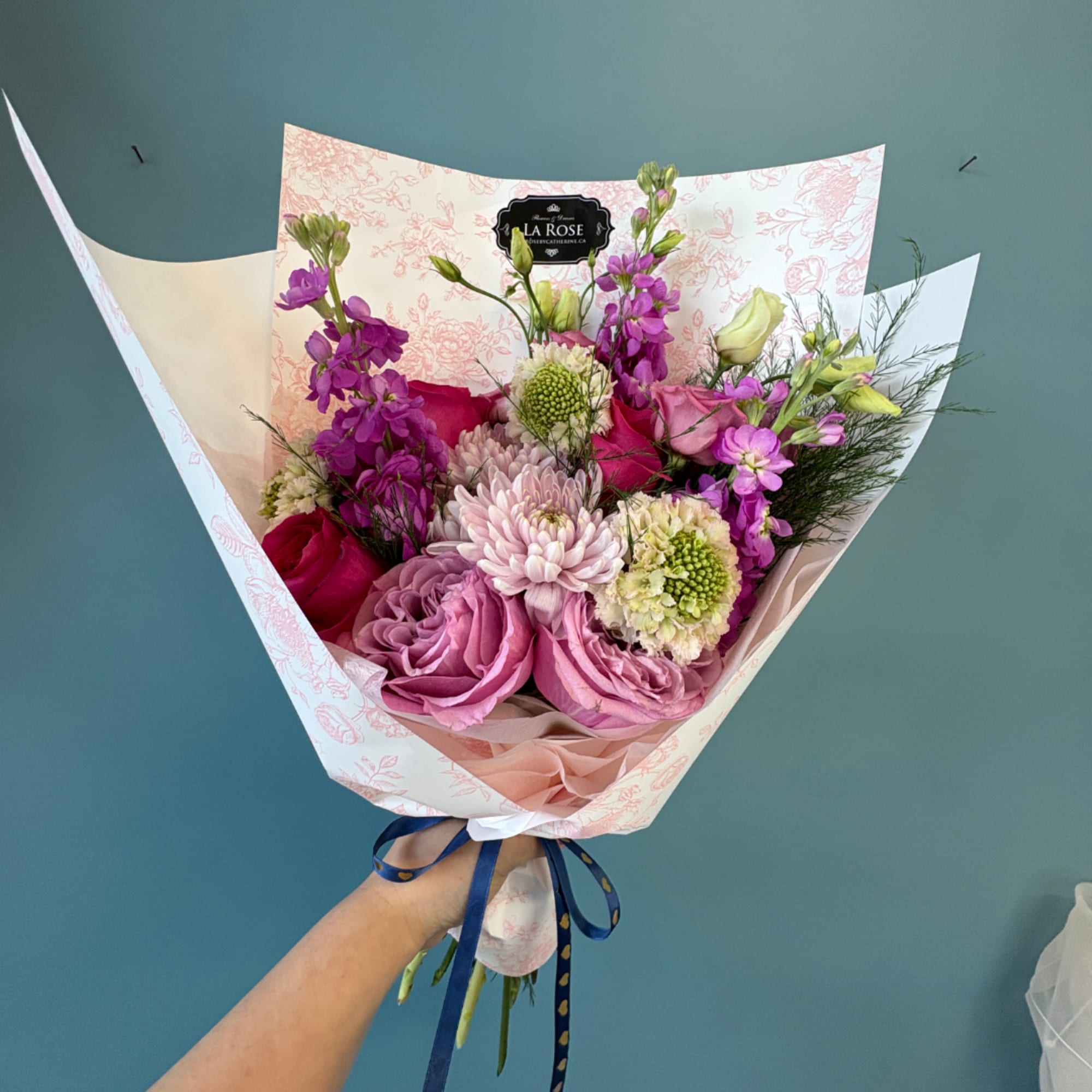 Handheld bouquet of pink and purple flowers wrapped in patterned paper