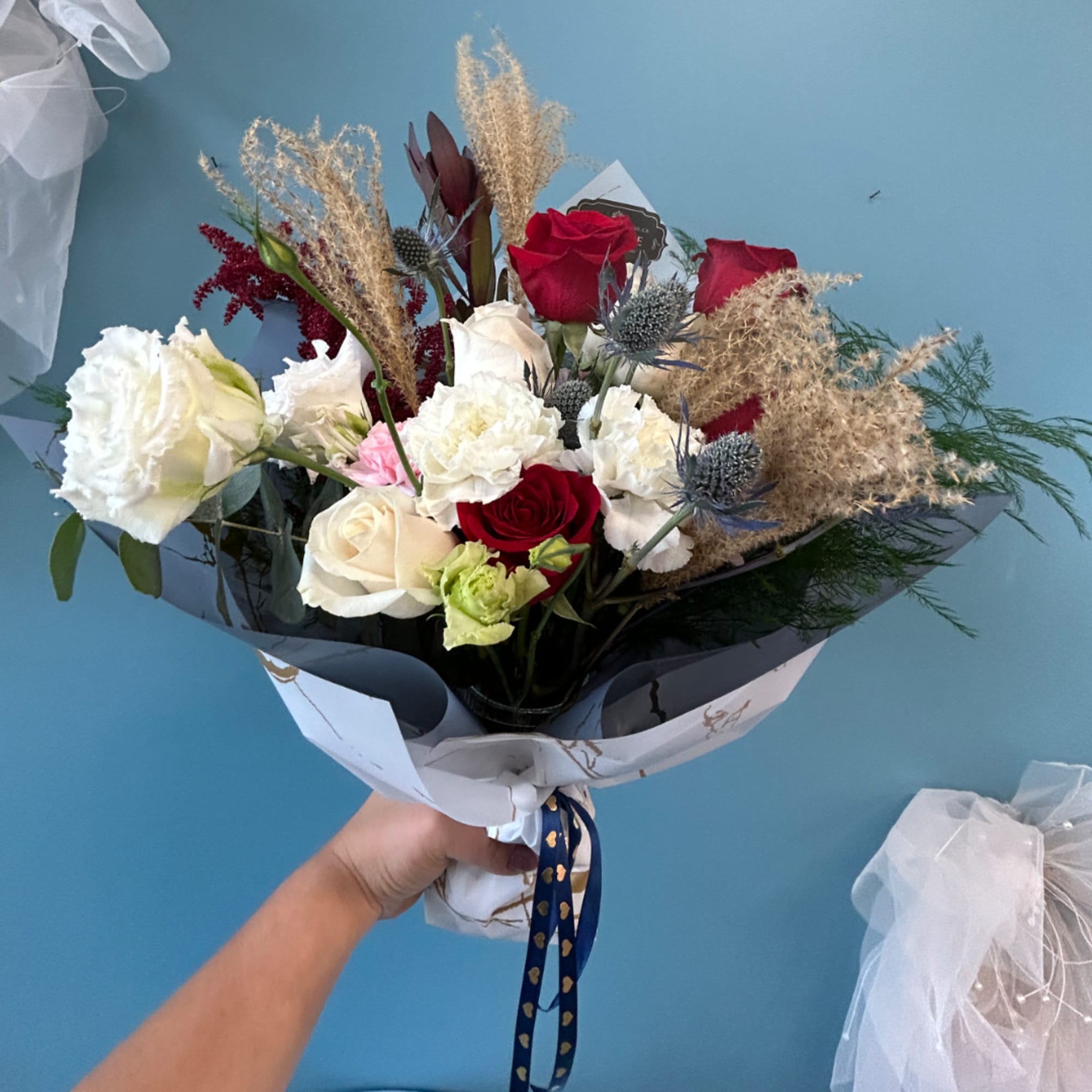 Handheld bouquet of red, white, and cream roses with dried grasses