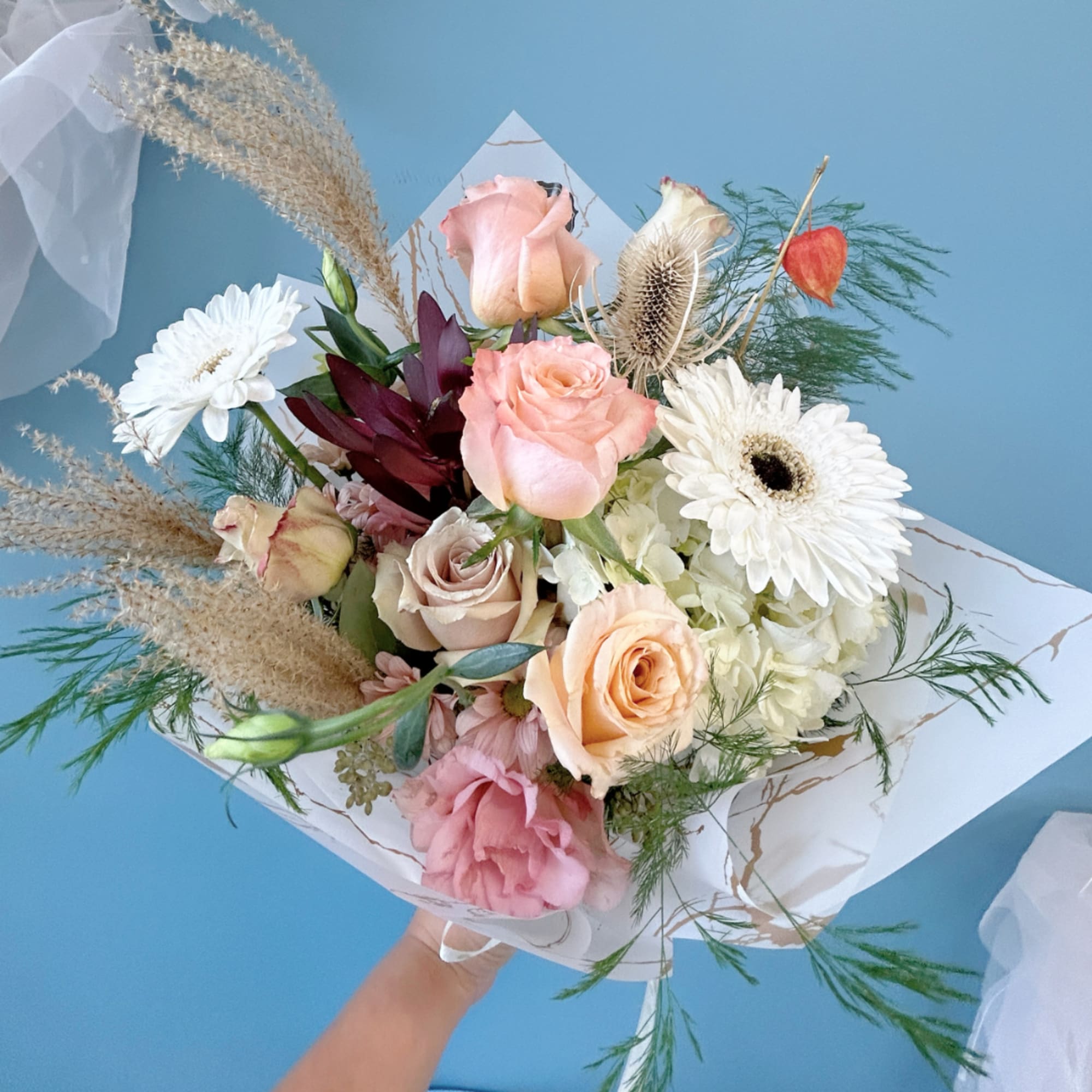 Handheld bouquet of pink and white roses with gerbera daisies and dried grasses