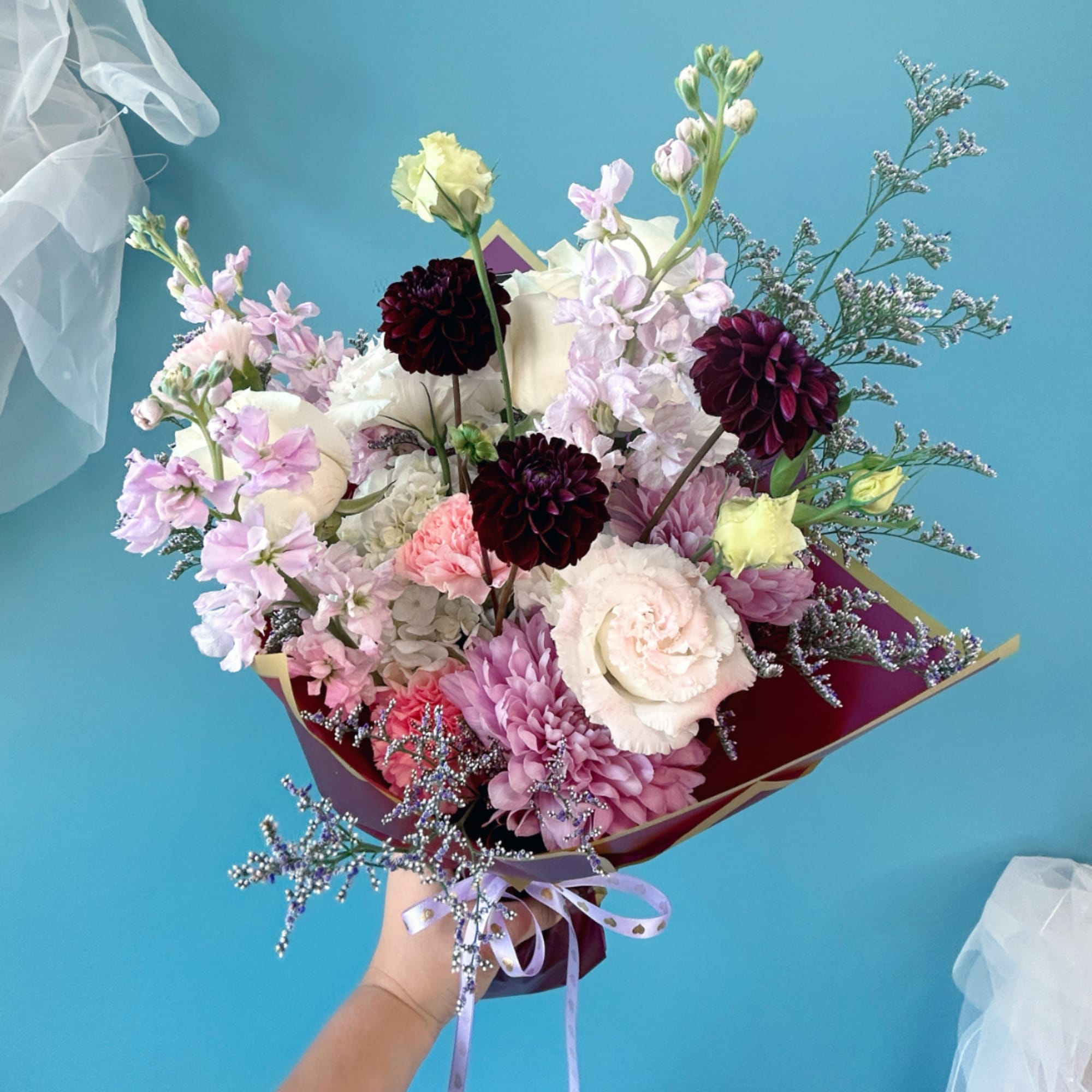 Handheld bouquet of pastel and dark blooms wrapped in burgundy paper