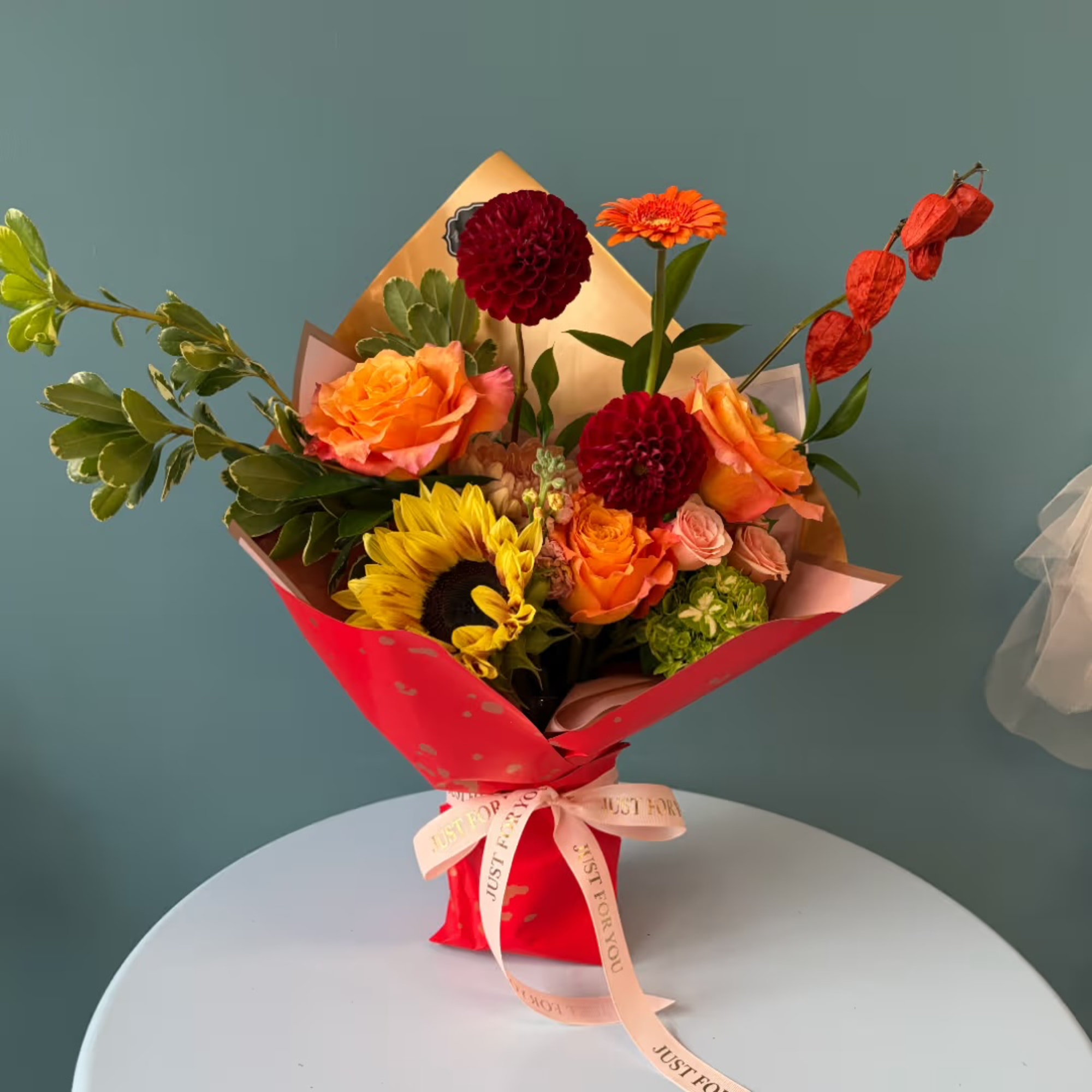 Bouquet of orange, red, and yellow flowers wrapped in red paper with a ribbon