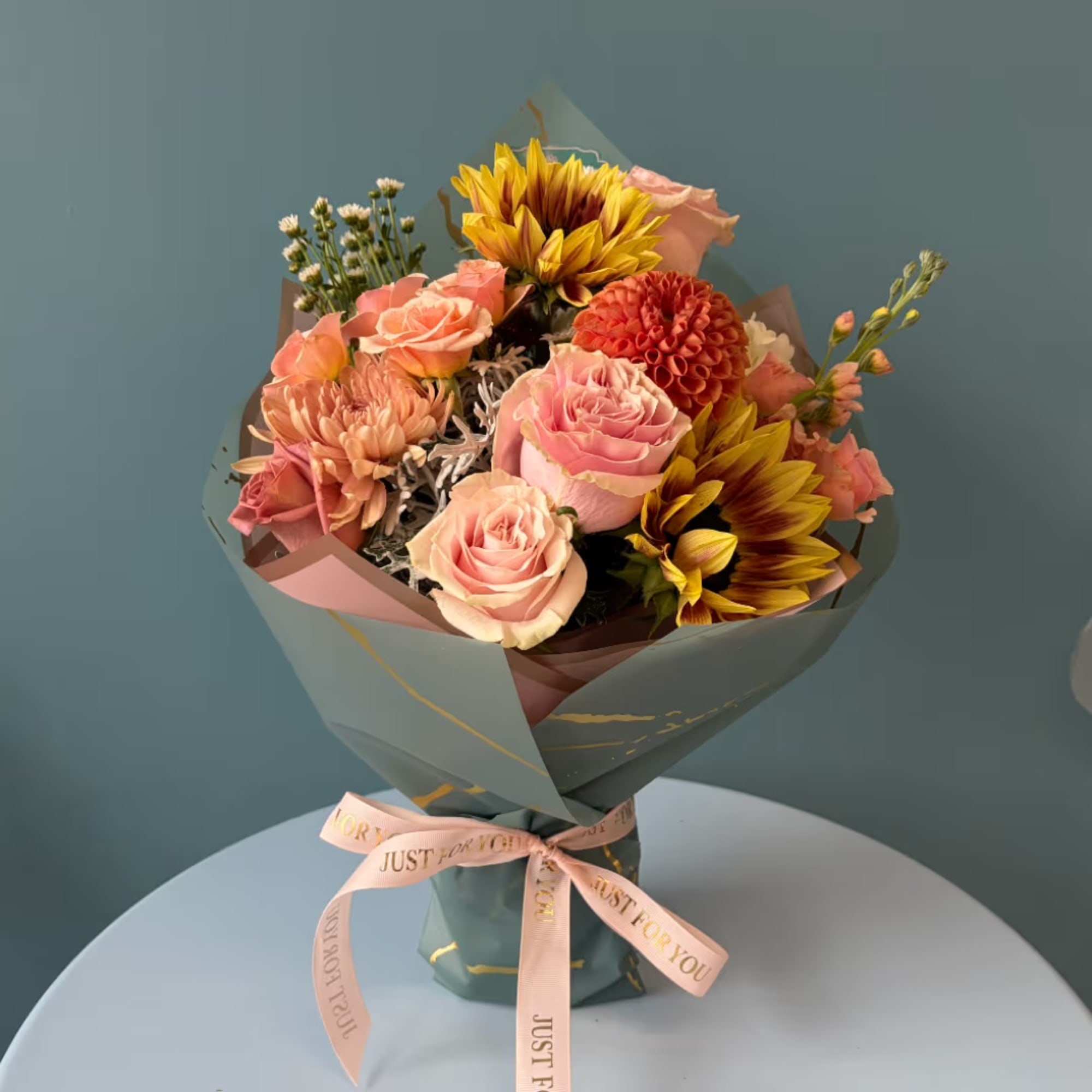 Bouquet of pink roses and sunflowers wrapped in teal paper with a pink ribbon