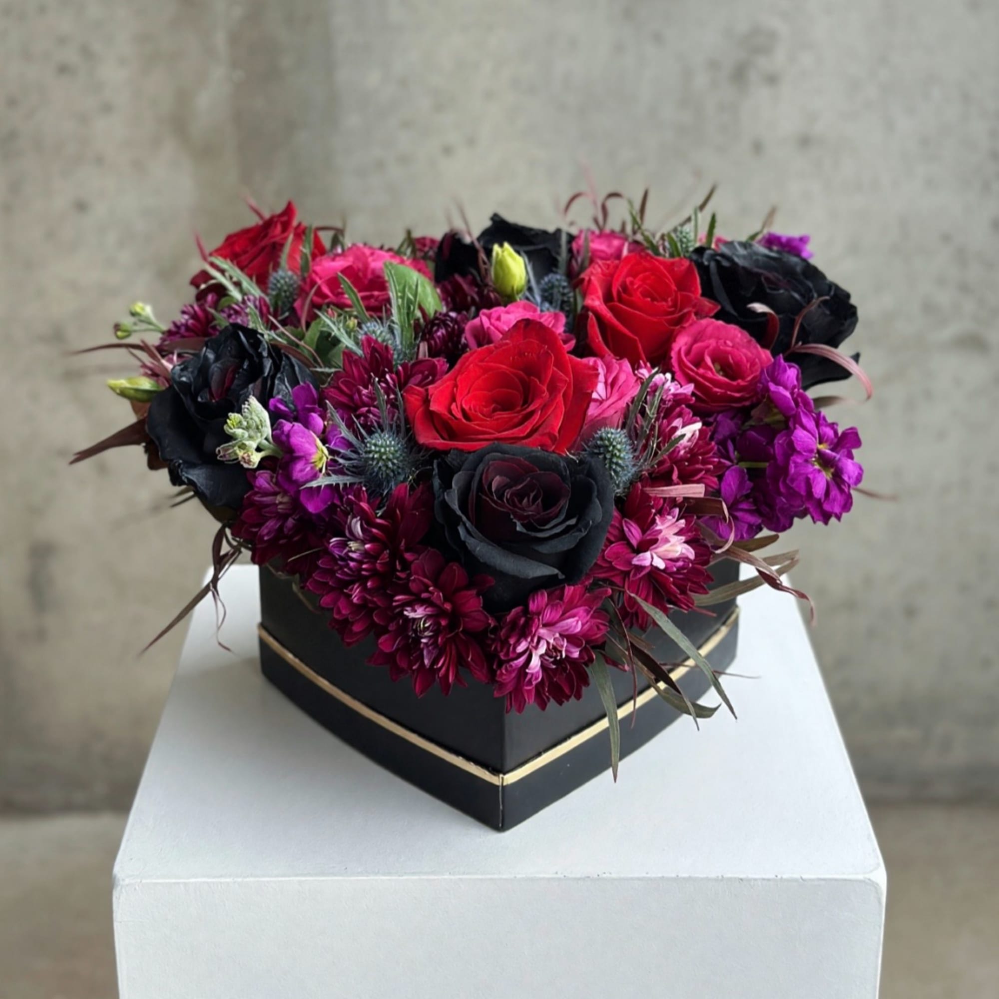 Heart-shaped box of red, pink, and black roses with purple flowers