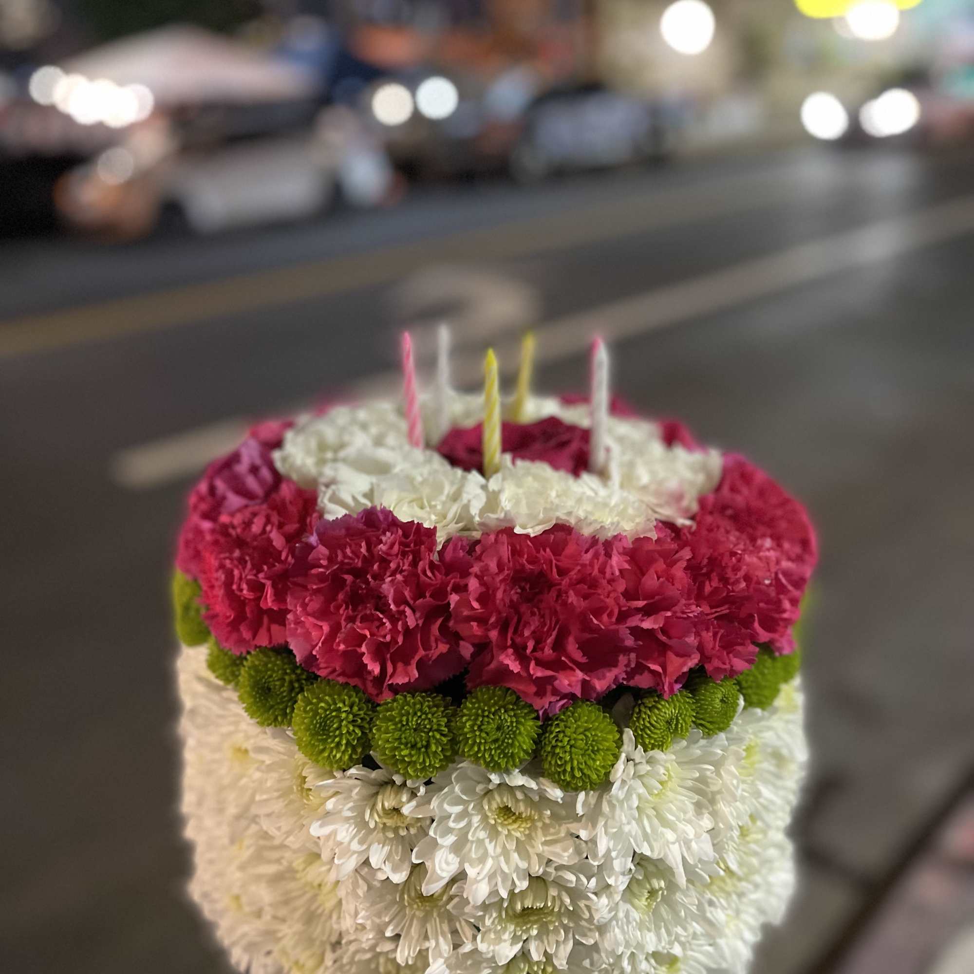 Round floral cake with pink, white, and green flowers and candles on top