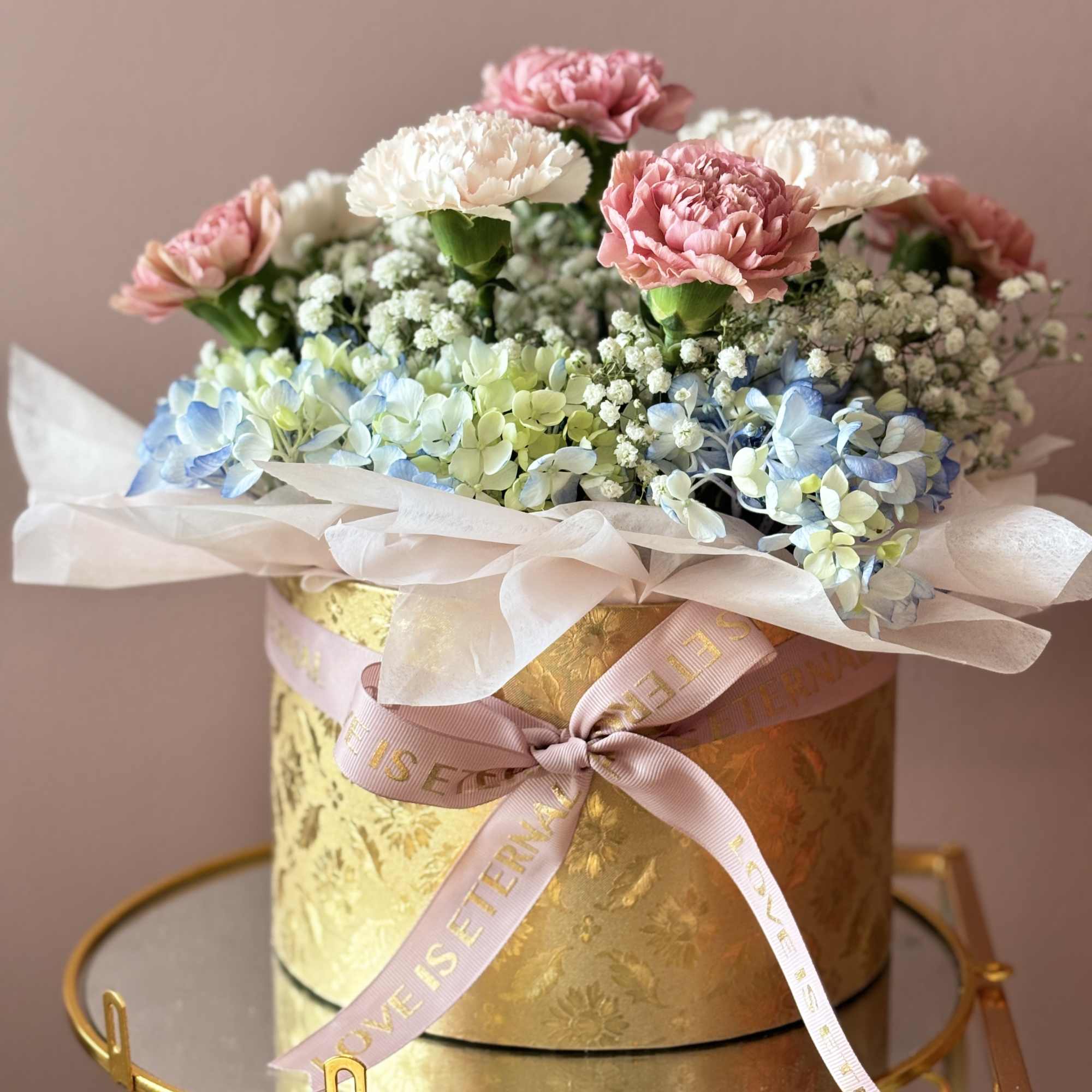 Pink and white carnations with blue hydrangeas in a gold box
