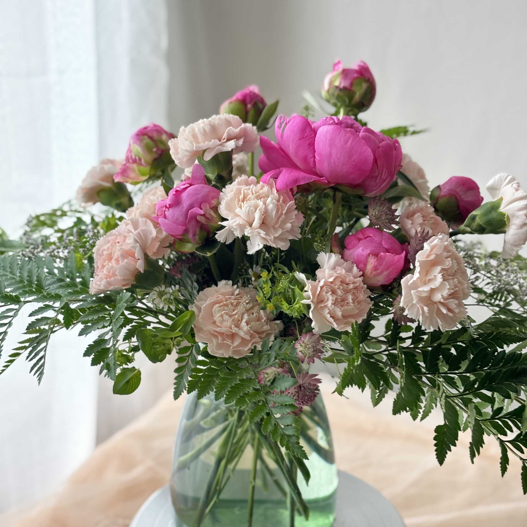Pink peonies and pale carnations in a green glass vase