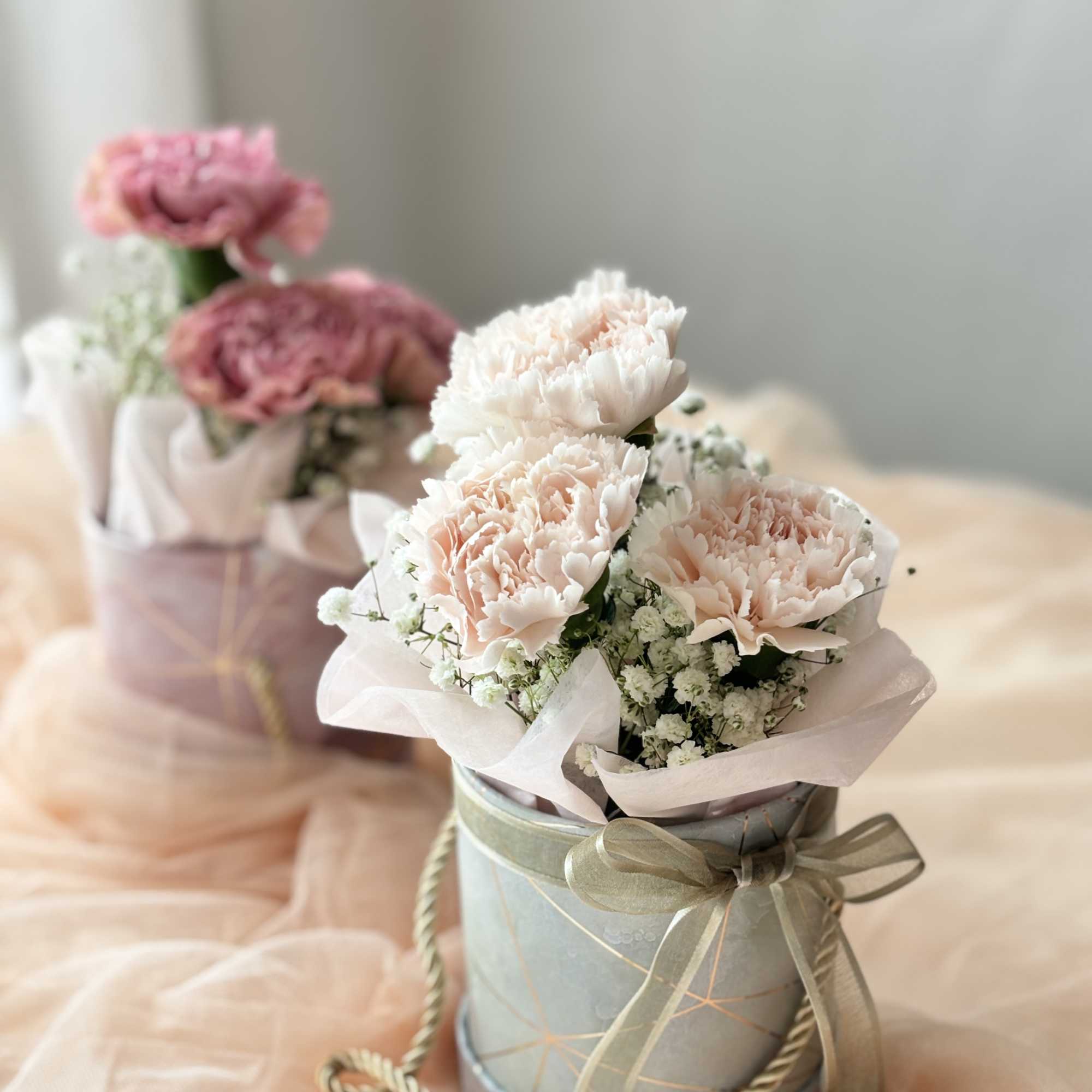 Pink carnations in a ribbon-tied gift box with baby's breath