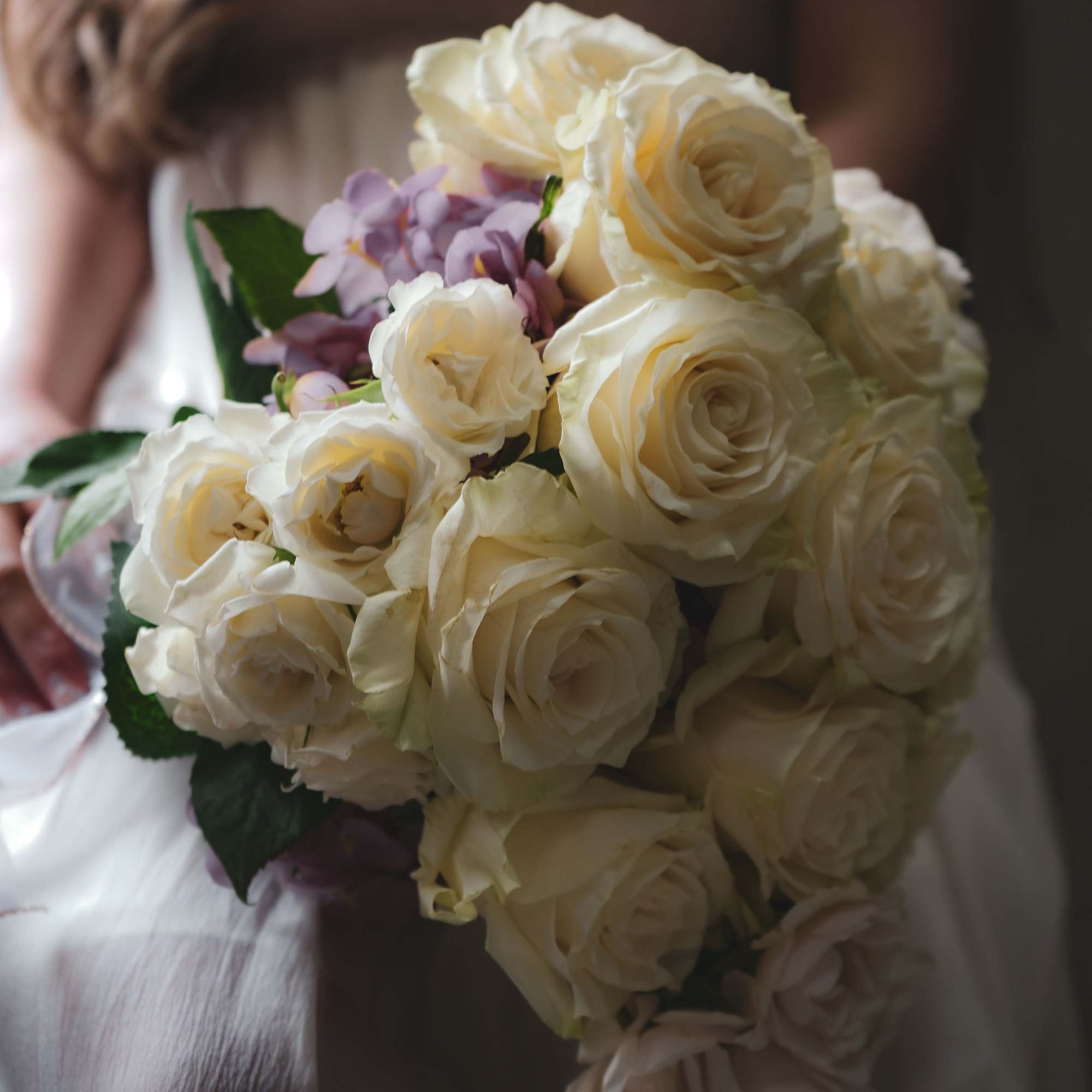 Bride holding a bouquet of cream roses and pale purple flowers
