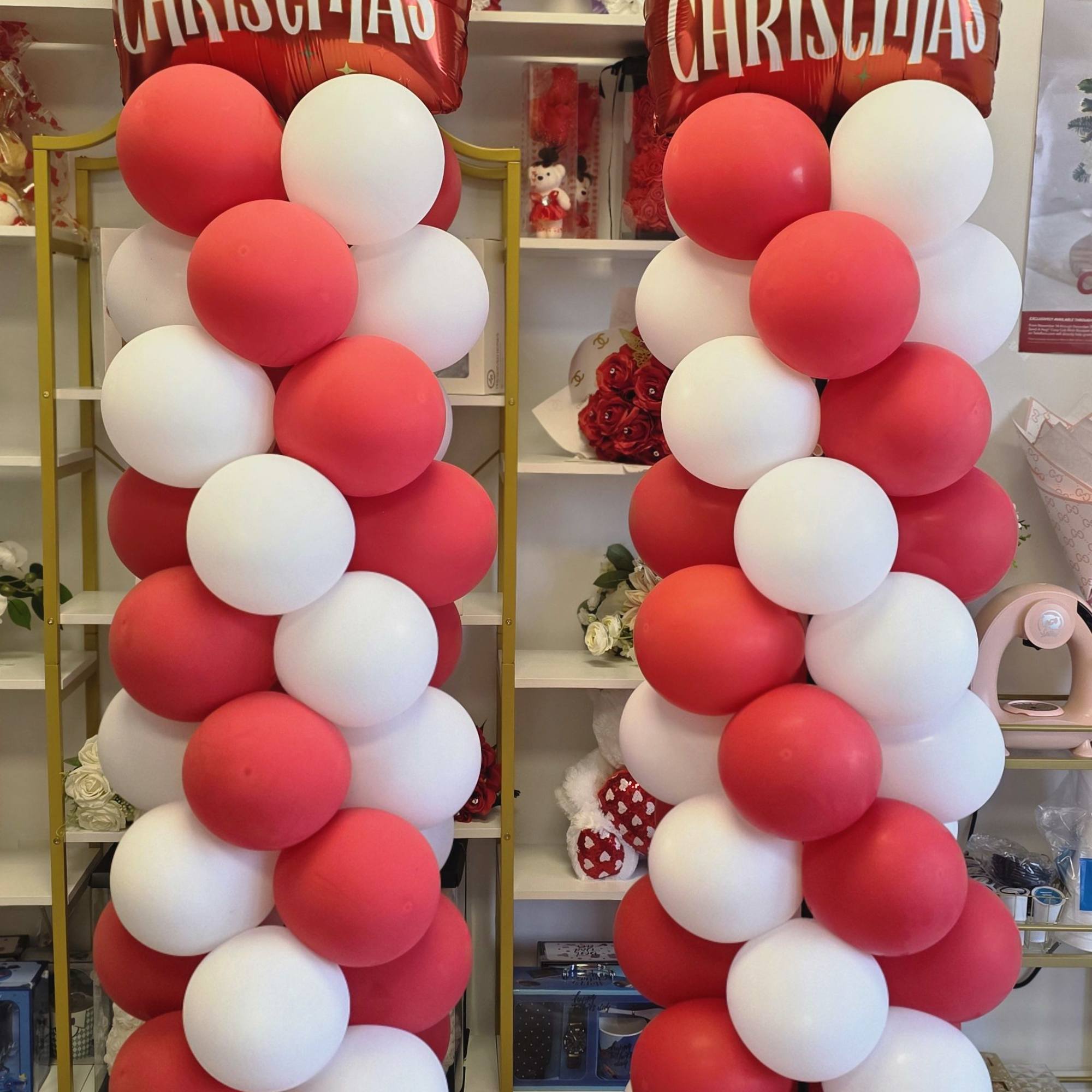 Two tall Christmas balloon columns with red and white balloons and Merry Christmas toppers