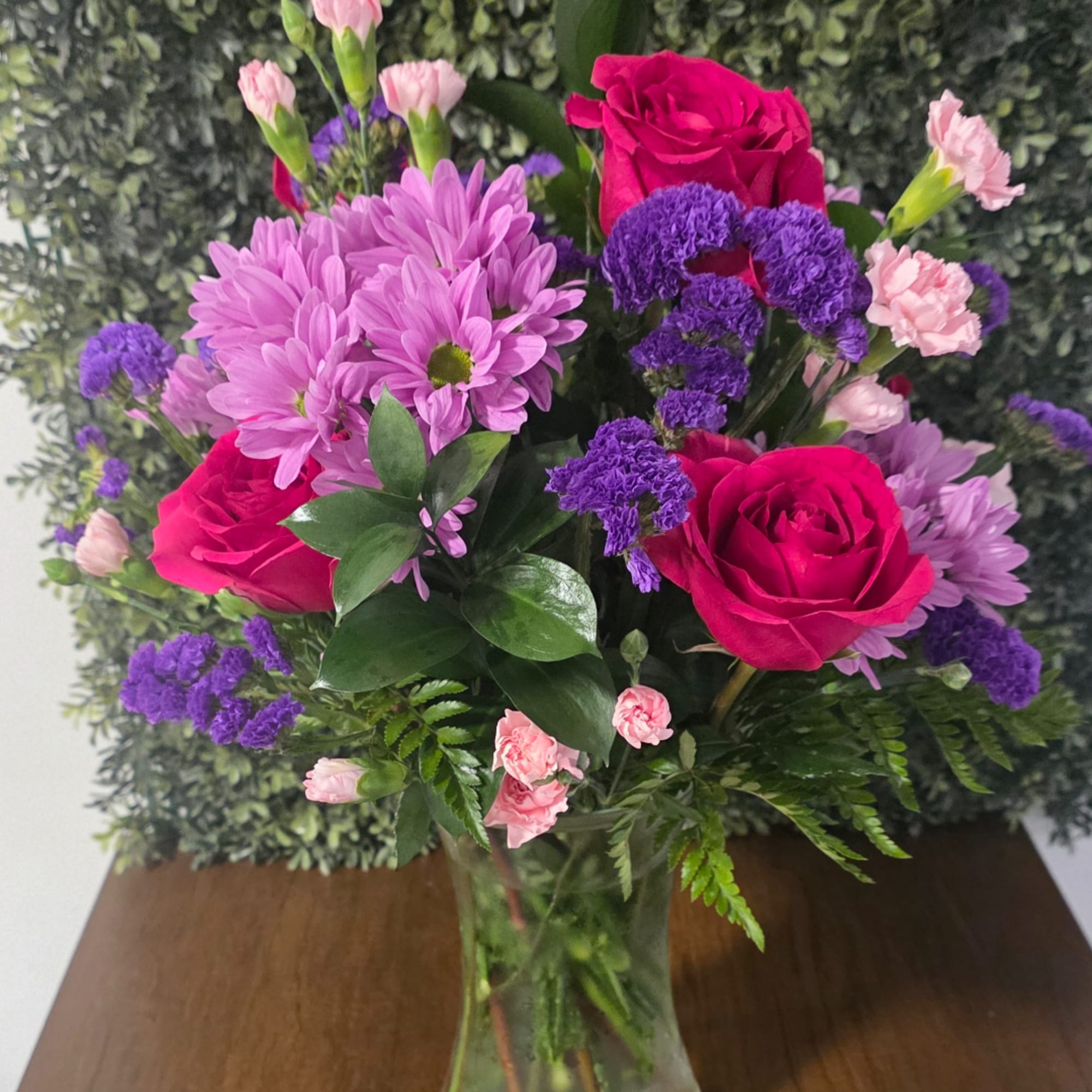 Bouquet of pink roses, purple flowers, and pink daisies in a glass vase