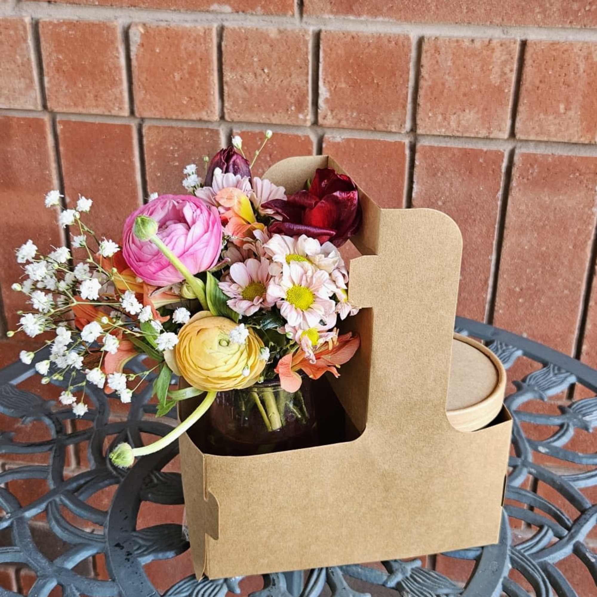 Mixed bouquet of pink, yellow, and red flowers in a kraft carrier