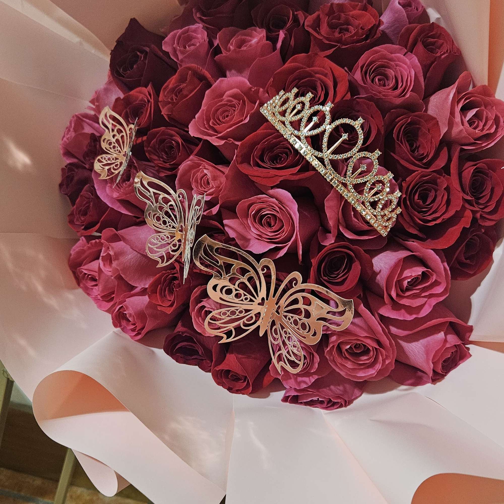 Bouquet of red and pink roses wrapped in pale pink paper with butterfly picks
