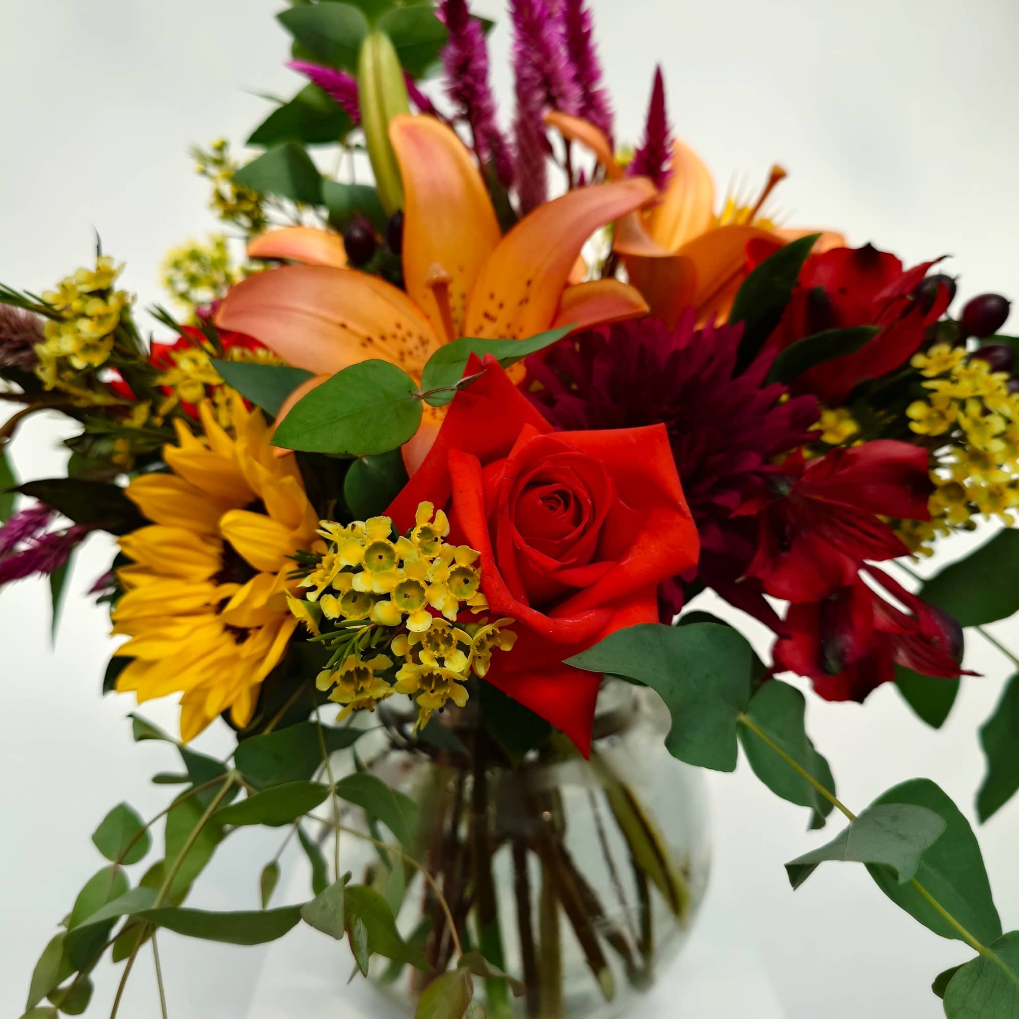 Mixed bouquet with red roses, orange lilies, and yellow blooms in a glass vase