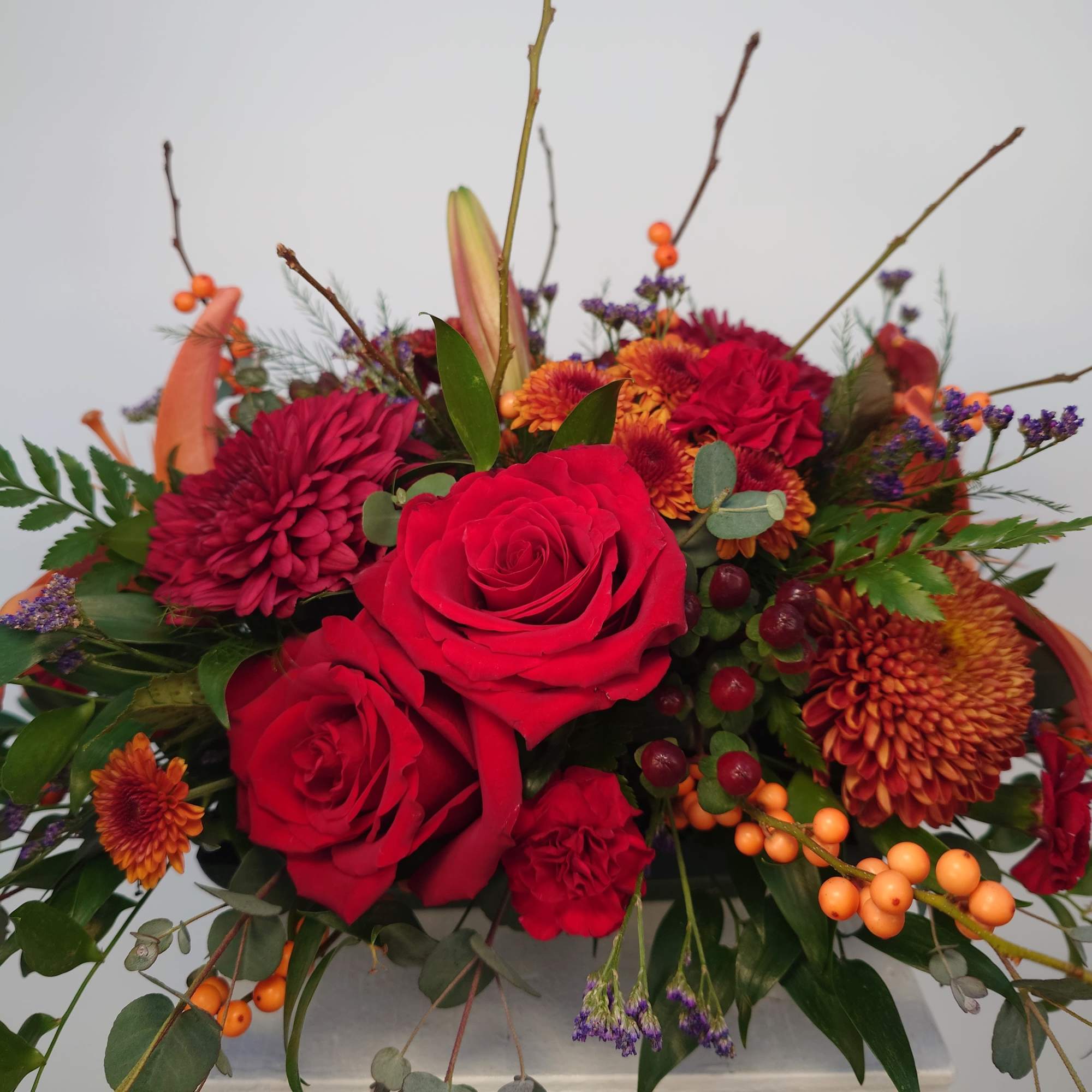 Red roses and burgundy mums in a low floral arrangement with orange berries
