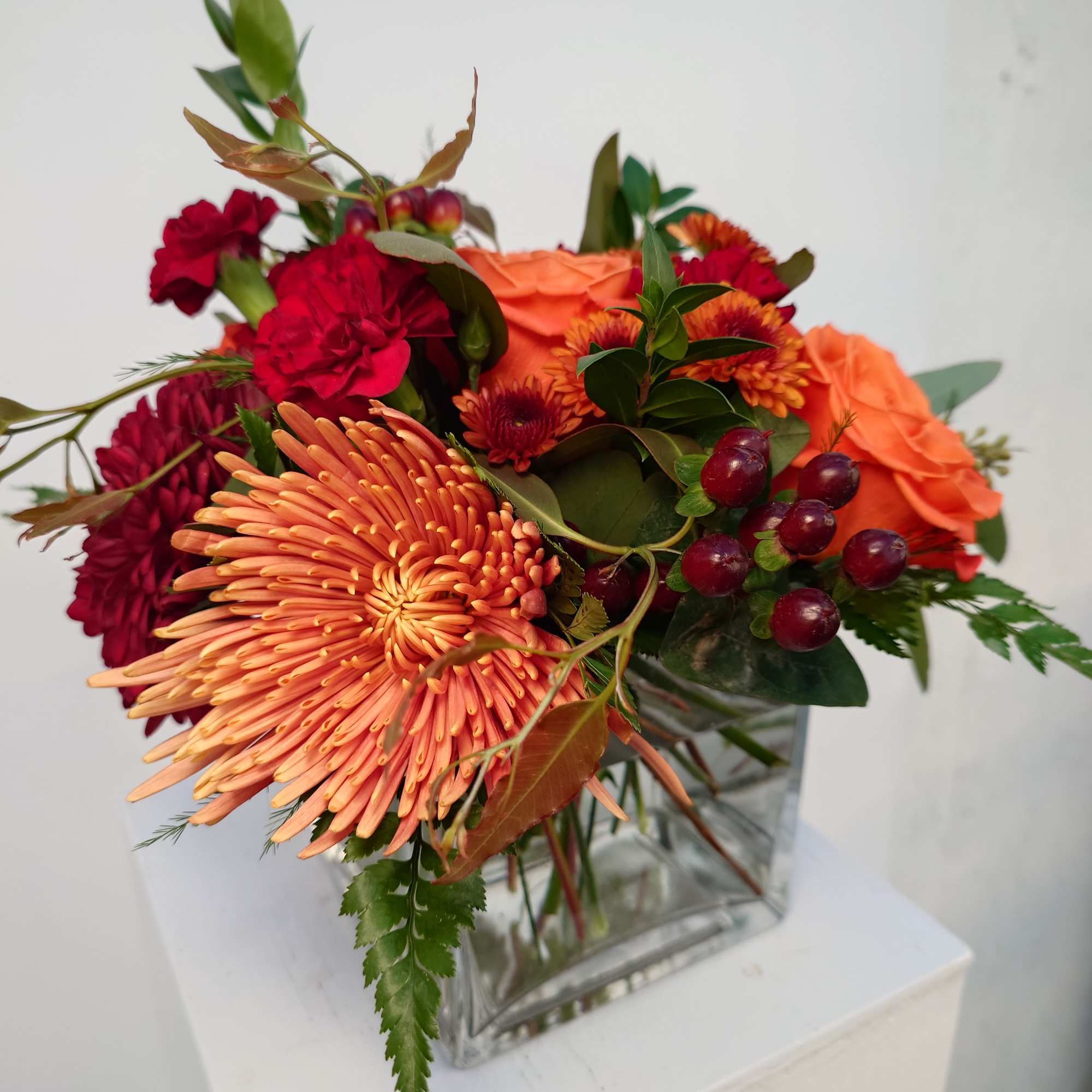 Orange and red mixed bouquet in a clear square vase