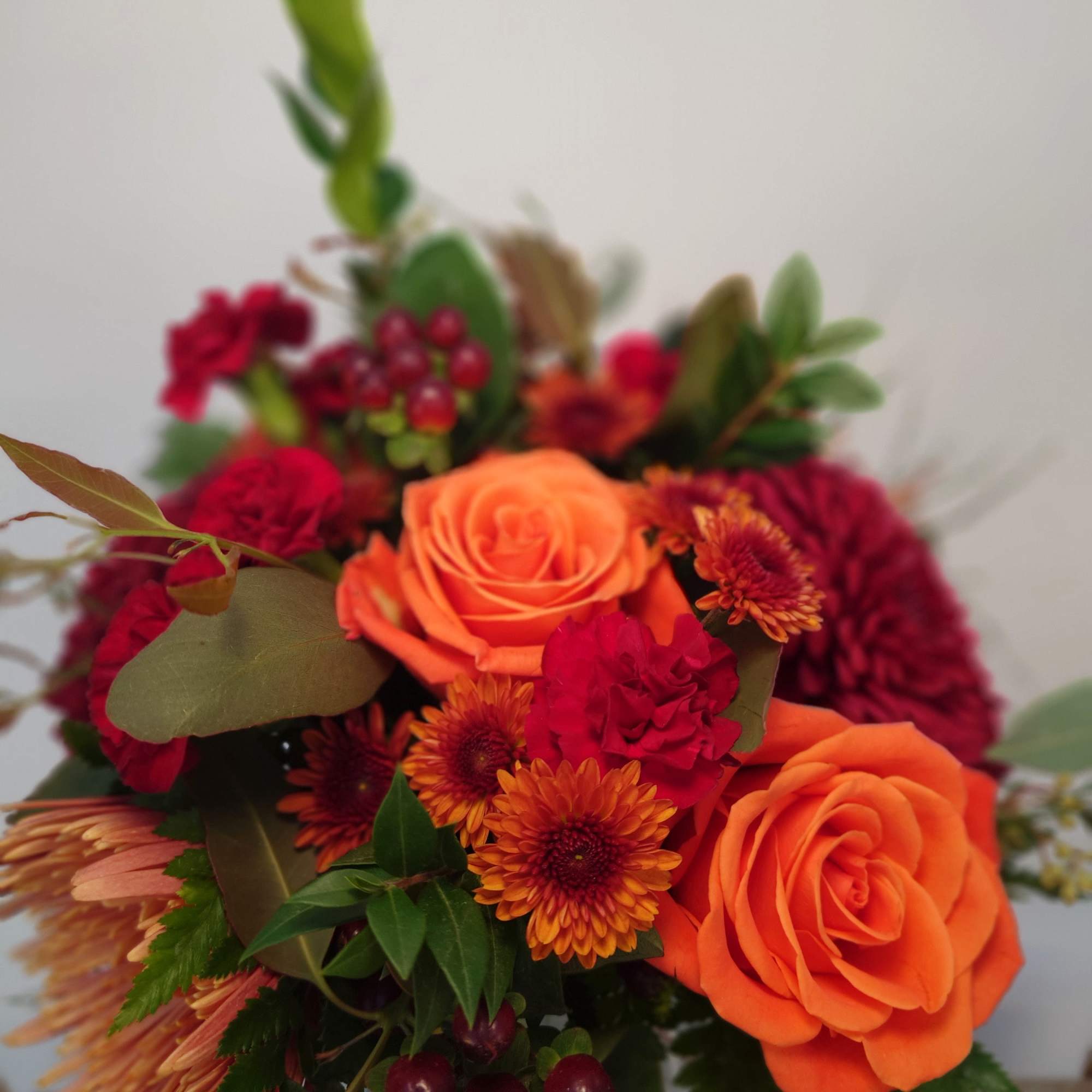 Bouquet of orange roses and red flowers with mixed greenery