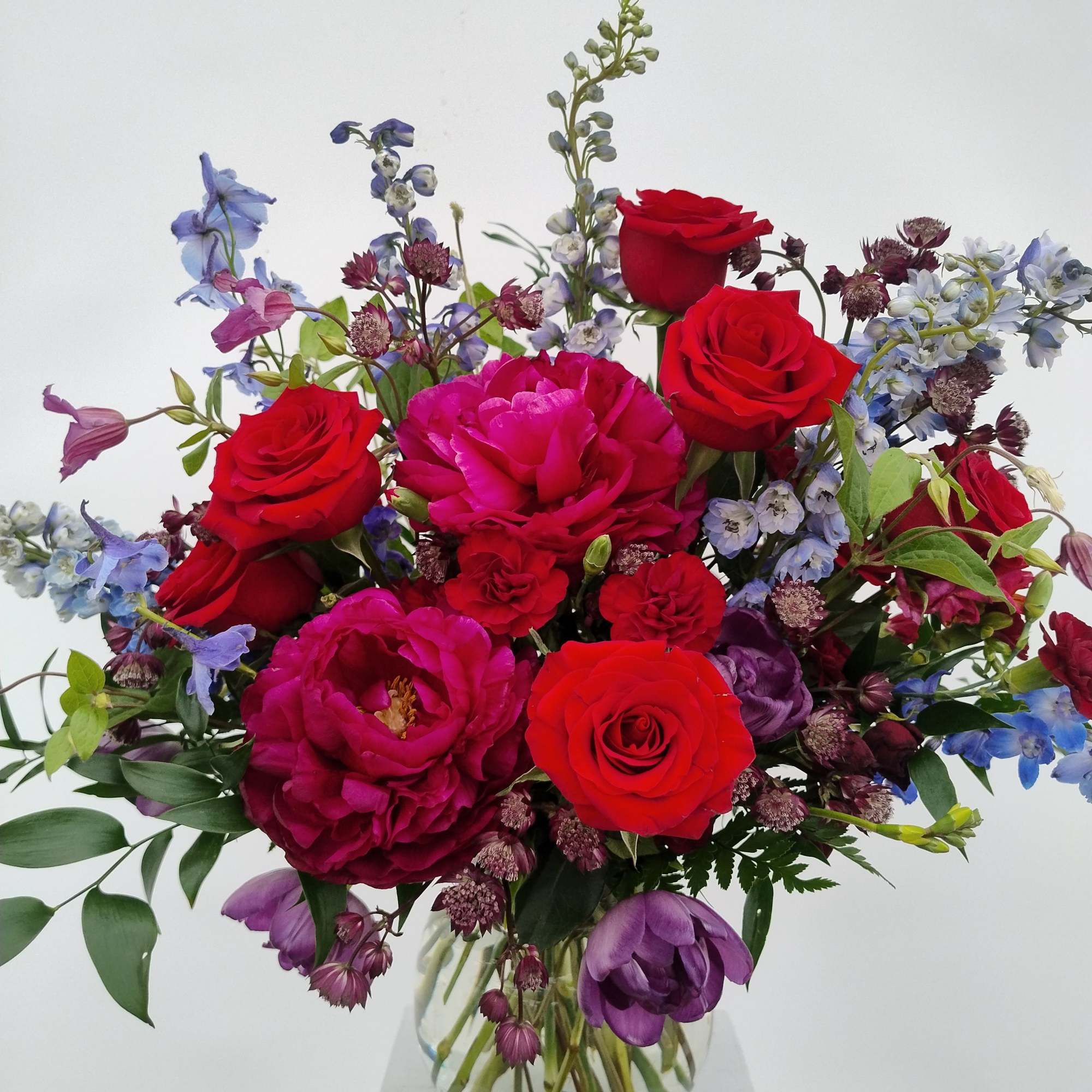 Bouquet of red roses and purple flowers in a clear glass vase