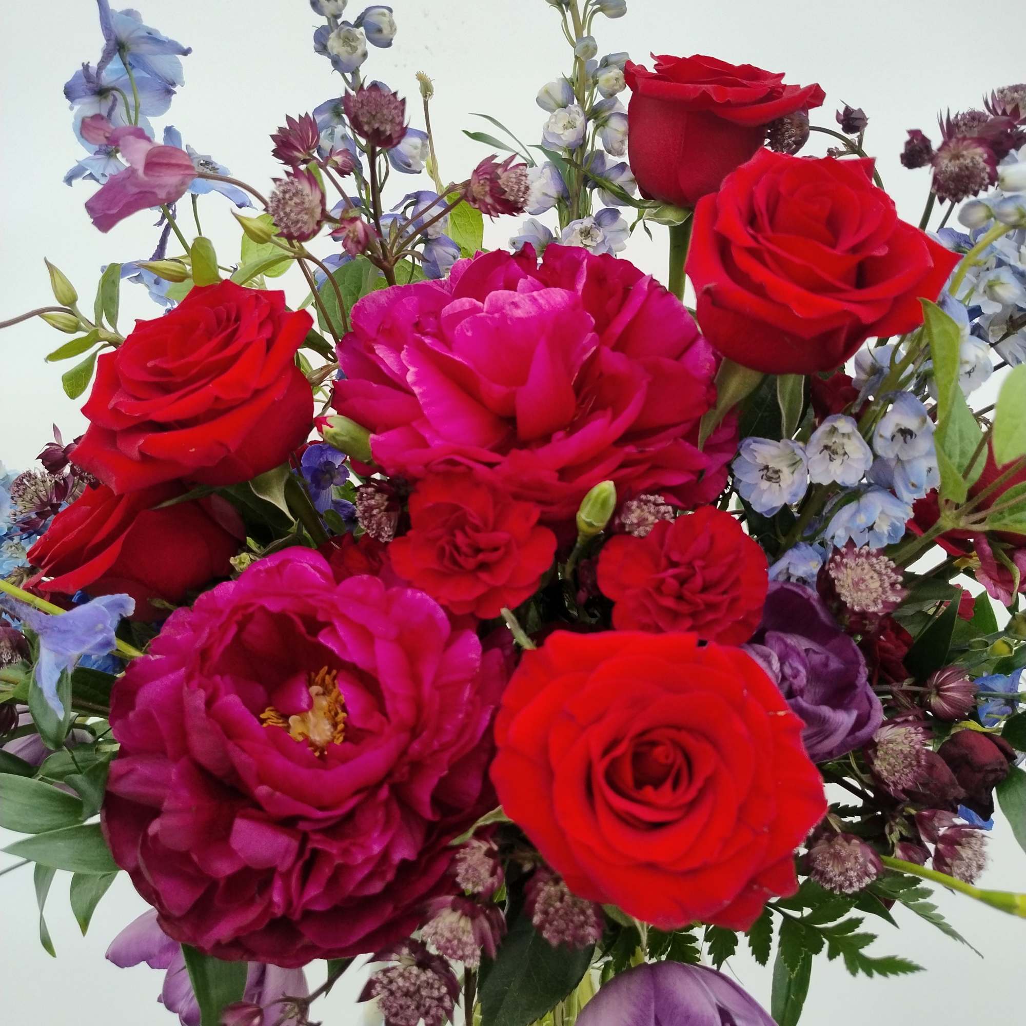 Bouquet of red and pink roses with purple and blue flowers in a glass vase