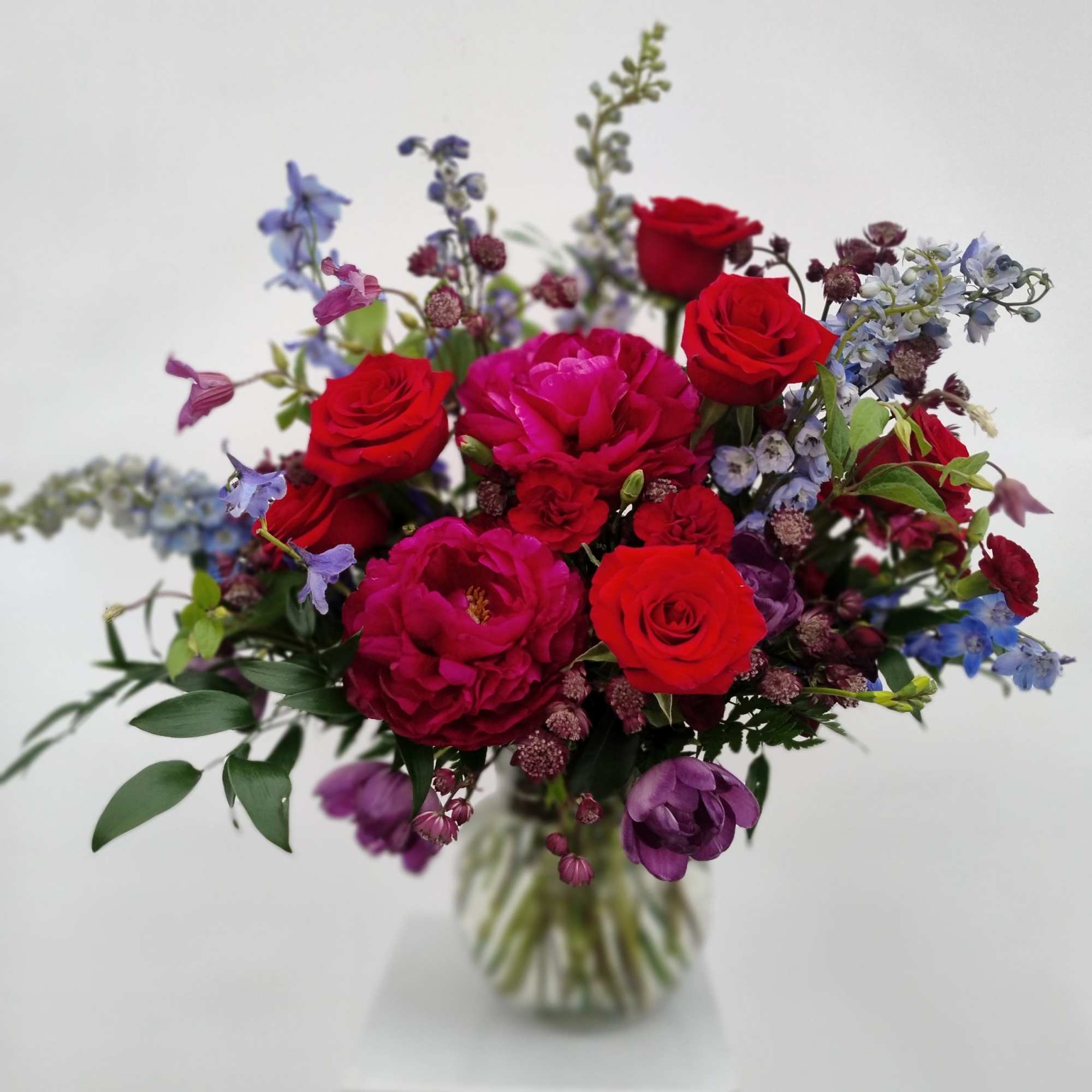 Bouquet of red and pink roses with purple flowers in a glass vase