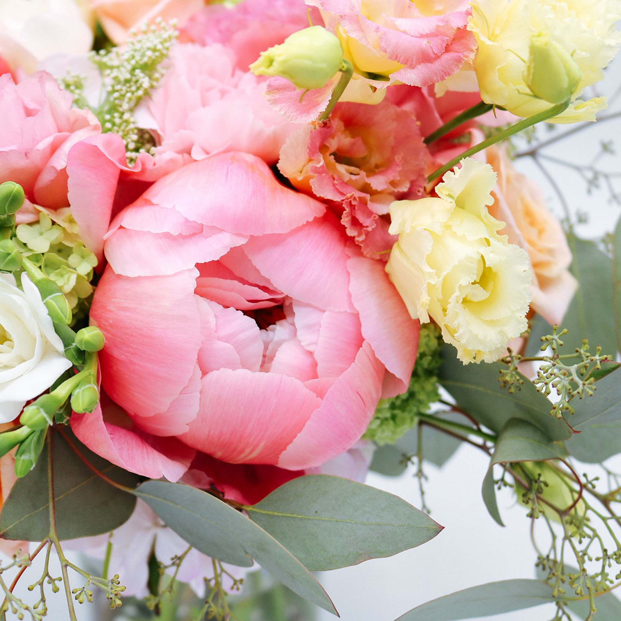 Close-up of a pastel bouquet with pink peony, yellow lisianthus, and white rose blooms