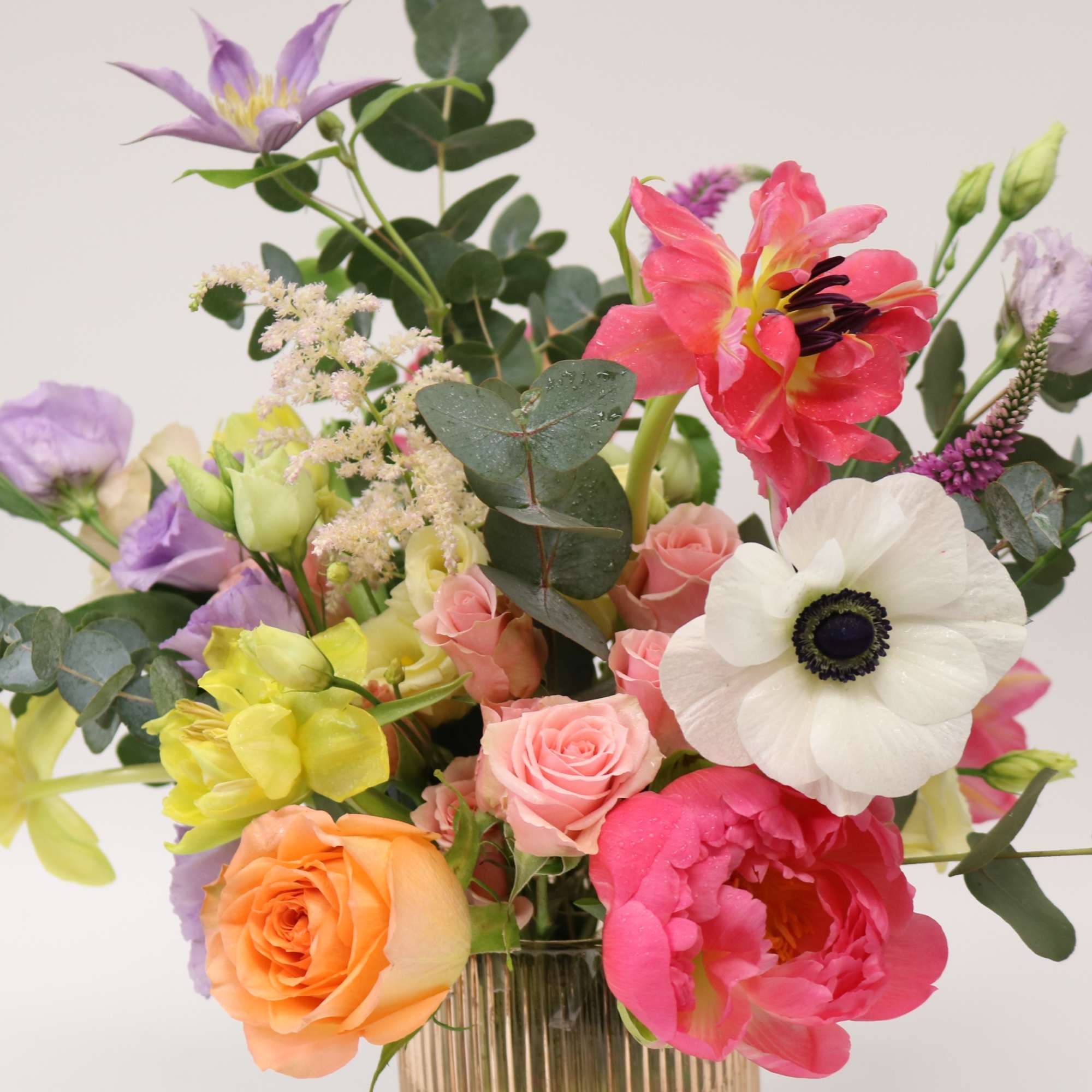 Mixed bouquet of roses, tulips, and anemones in a glass vase