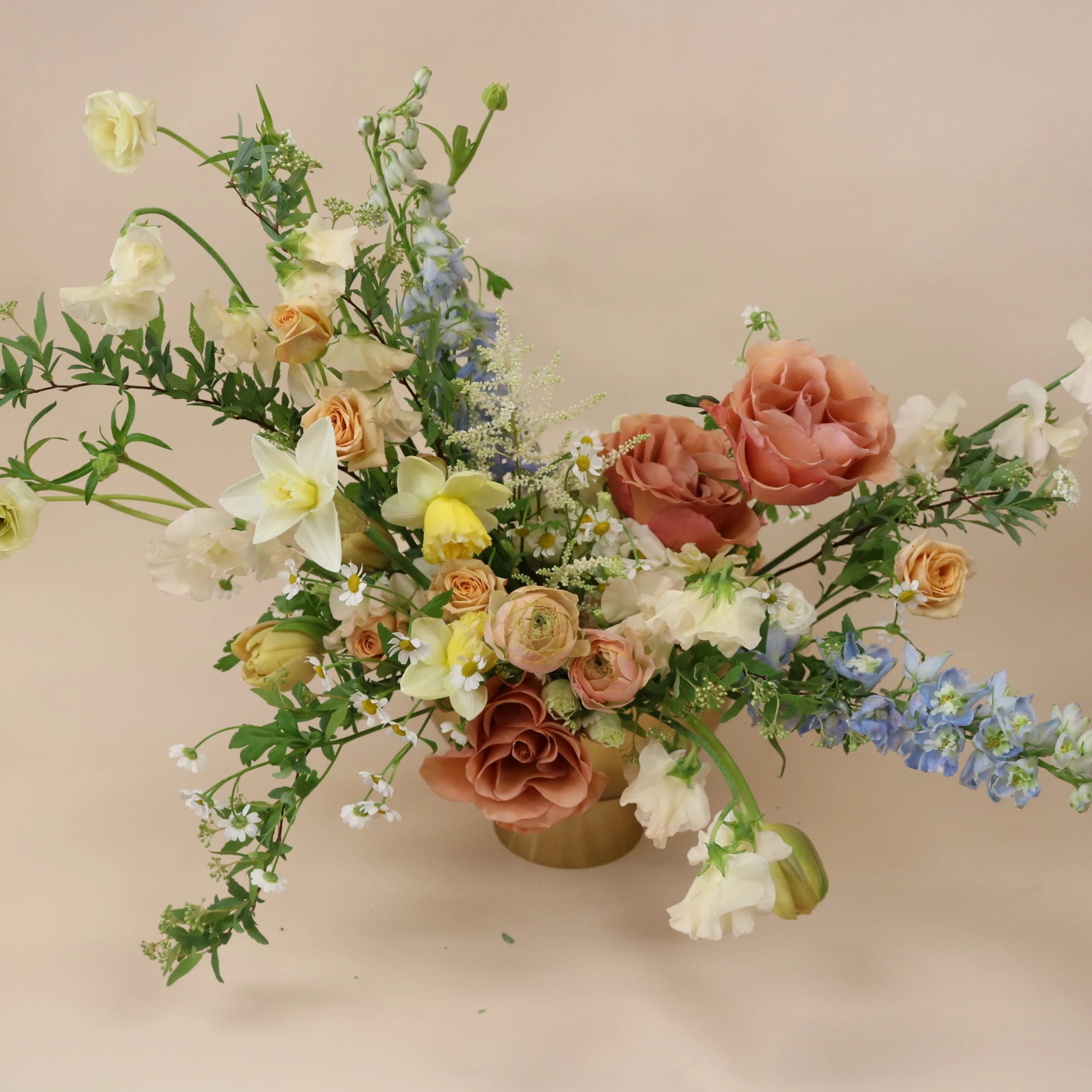 Loose floral arrangement in a gold vase with peach, white, and blue blooms