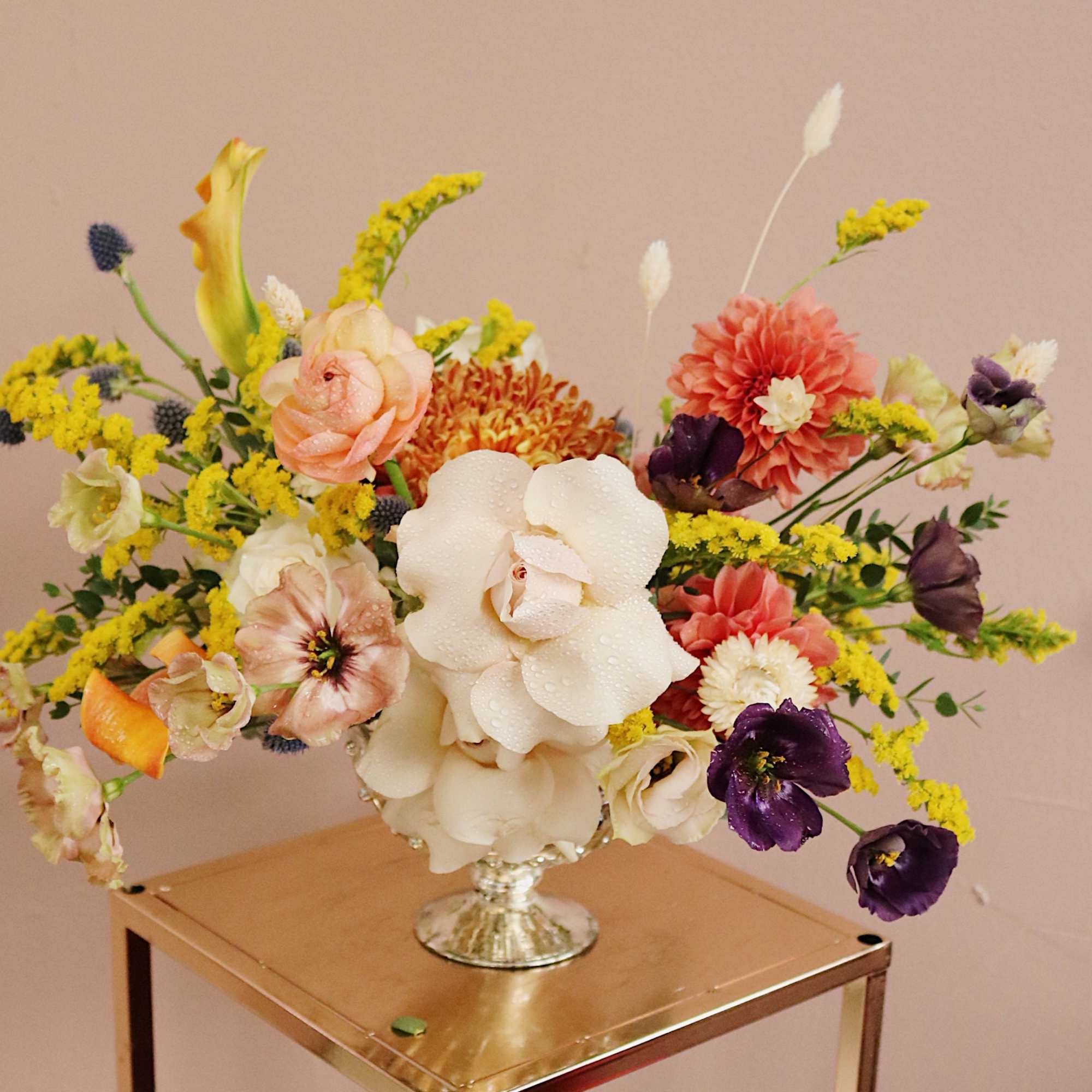 Mixed floral arrangement in a silver vase with white, peach, yellow, and purple blooms