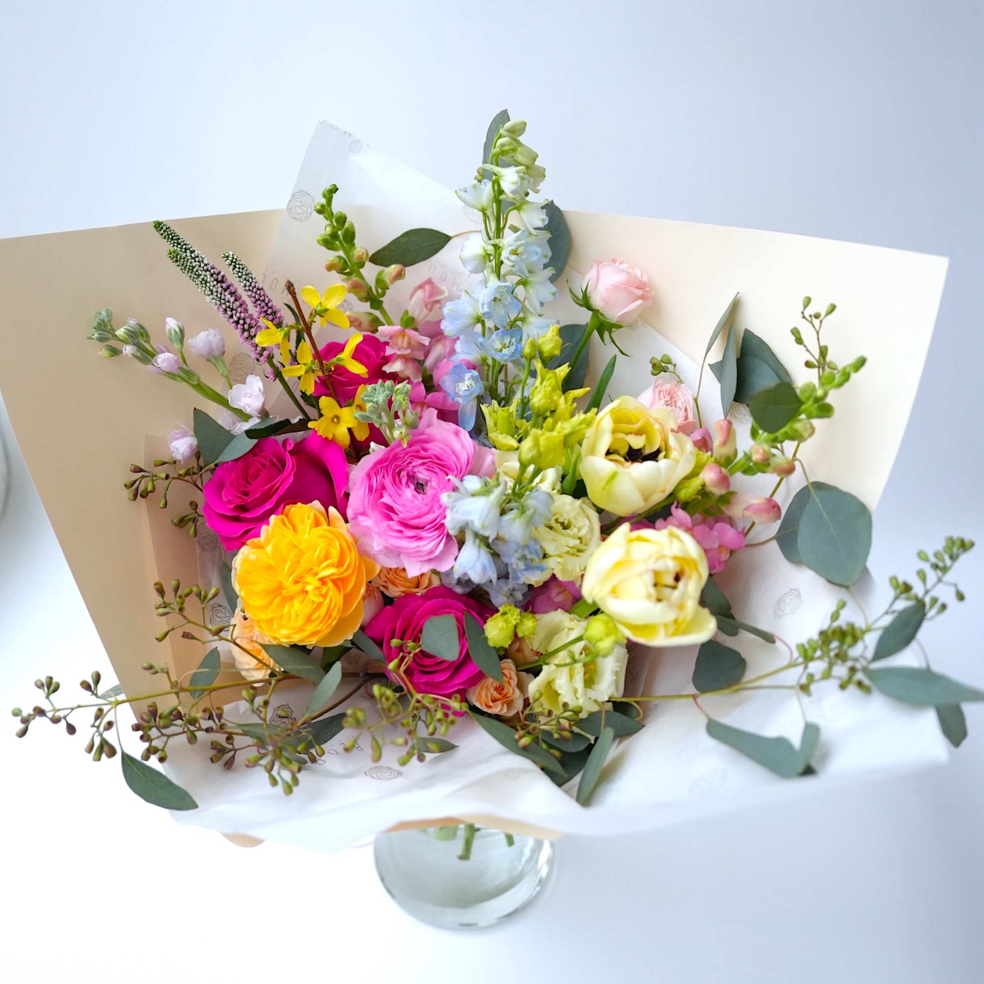 Mixed bouquet of colorful flowers in white wrapping with a glass vase