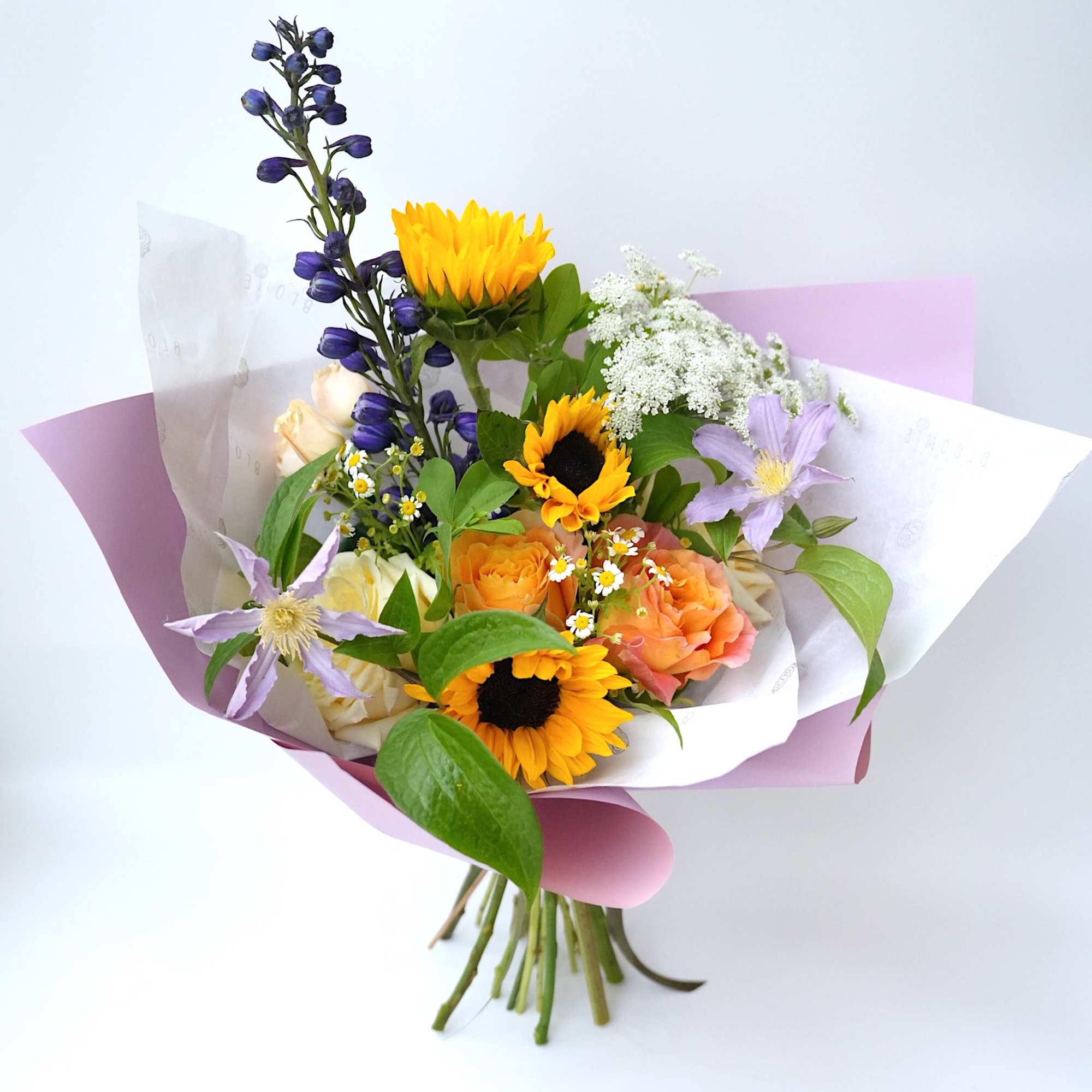 Mixed bouquet with sunflowers, roses, and purple flowers wrapped in pink paper