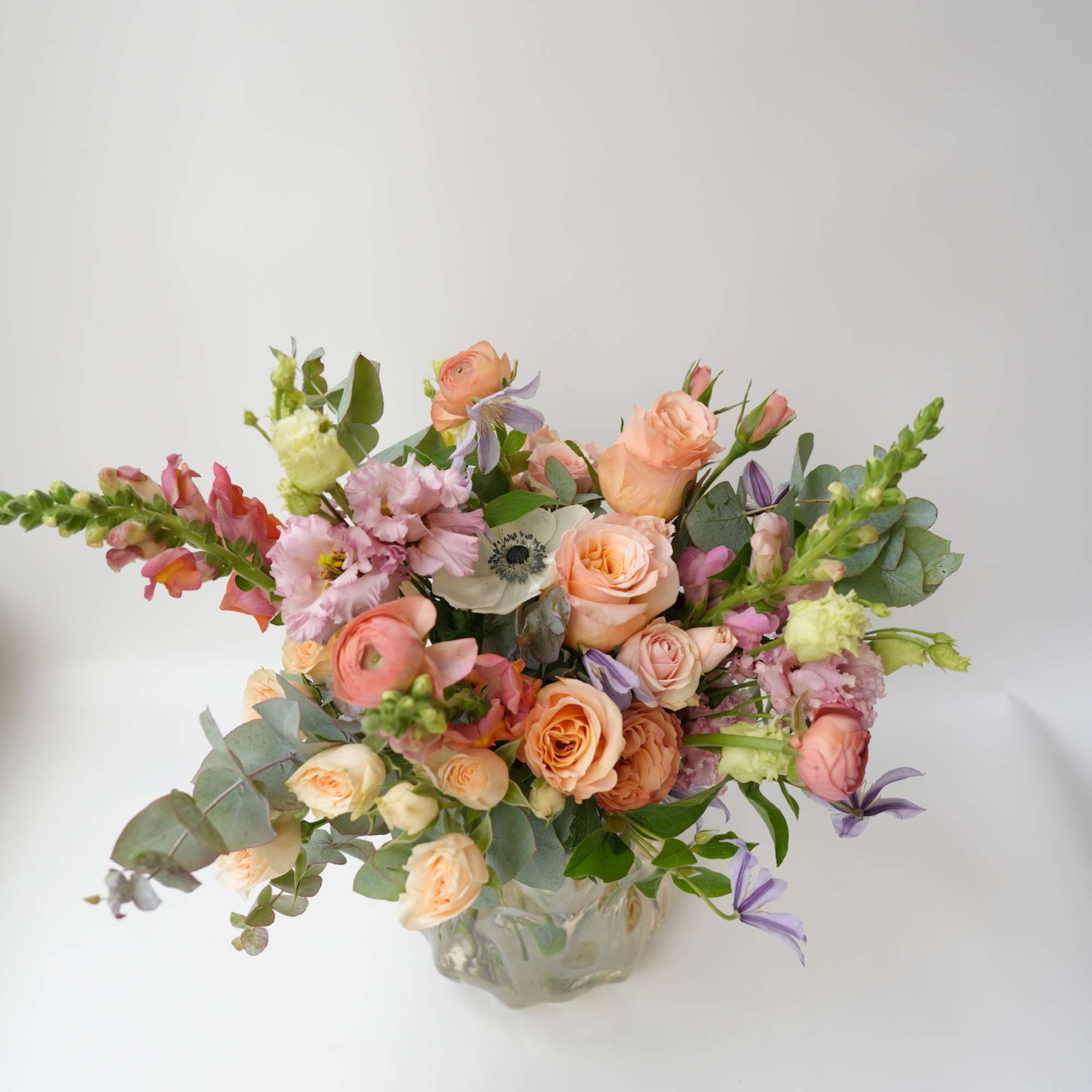 Mixed bouquet of peach, pink, and lavender flowers in a glass vase
