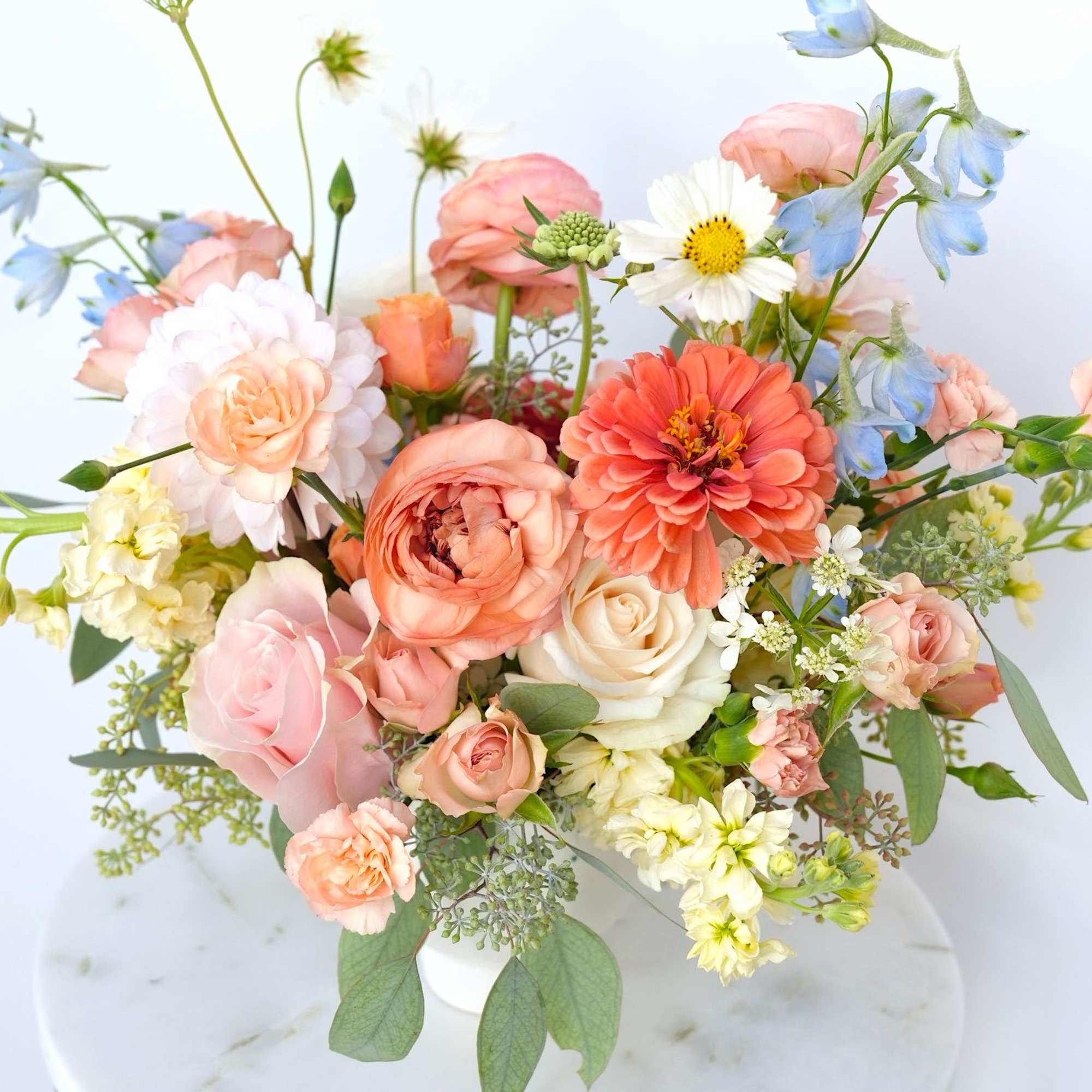 Pastel bouquet of roses, zinnias, and blue delphinium in a white vase