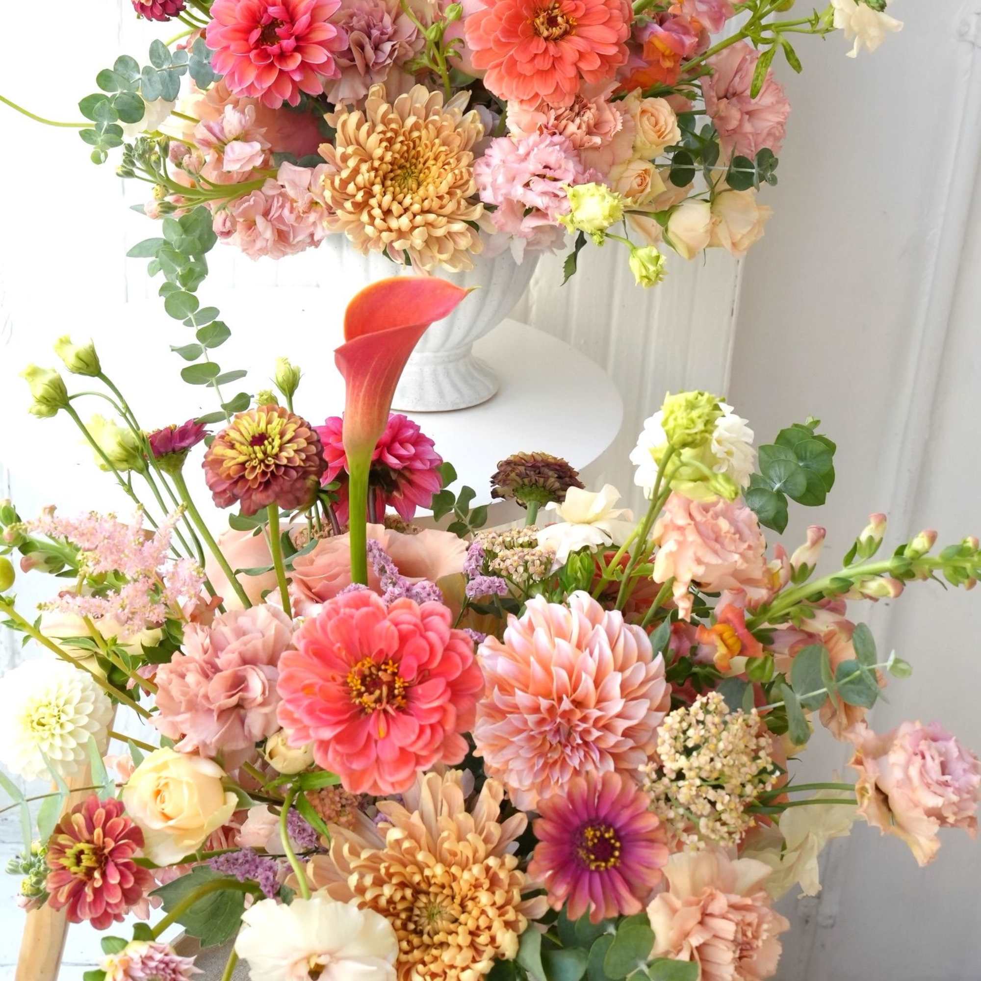 Two pastel floral arrangements in white vases with pink and peach blooms