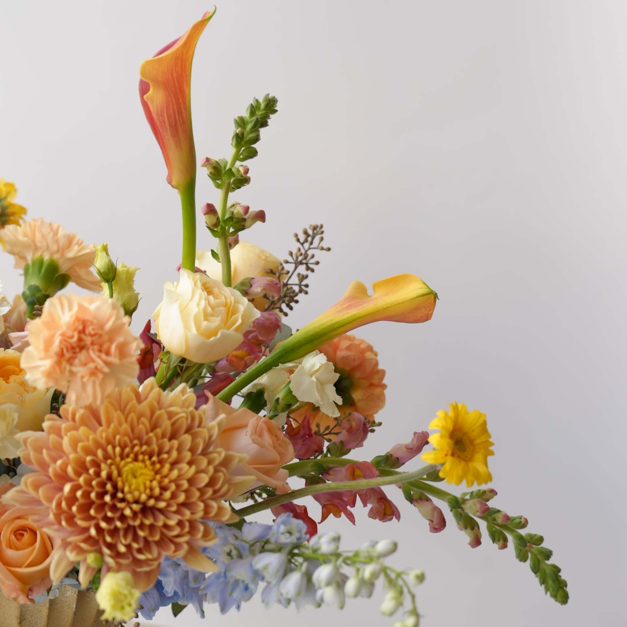 Mixed floral arrangement with calla lilies, chrysanthemums, and roses in a gold vase