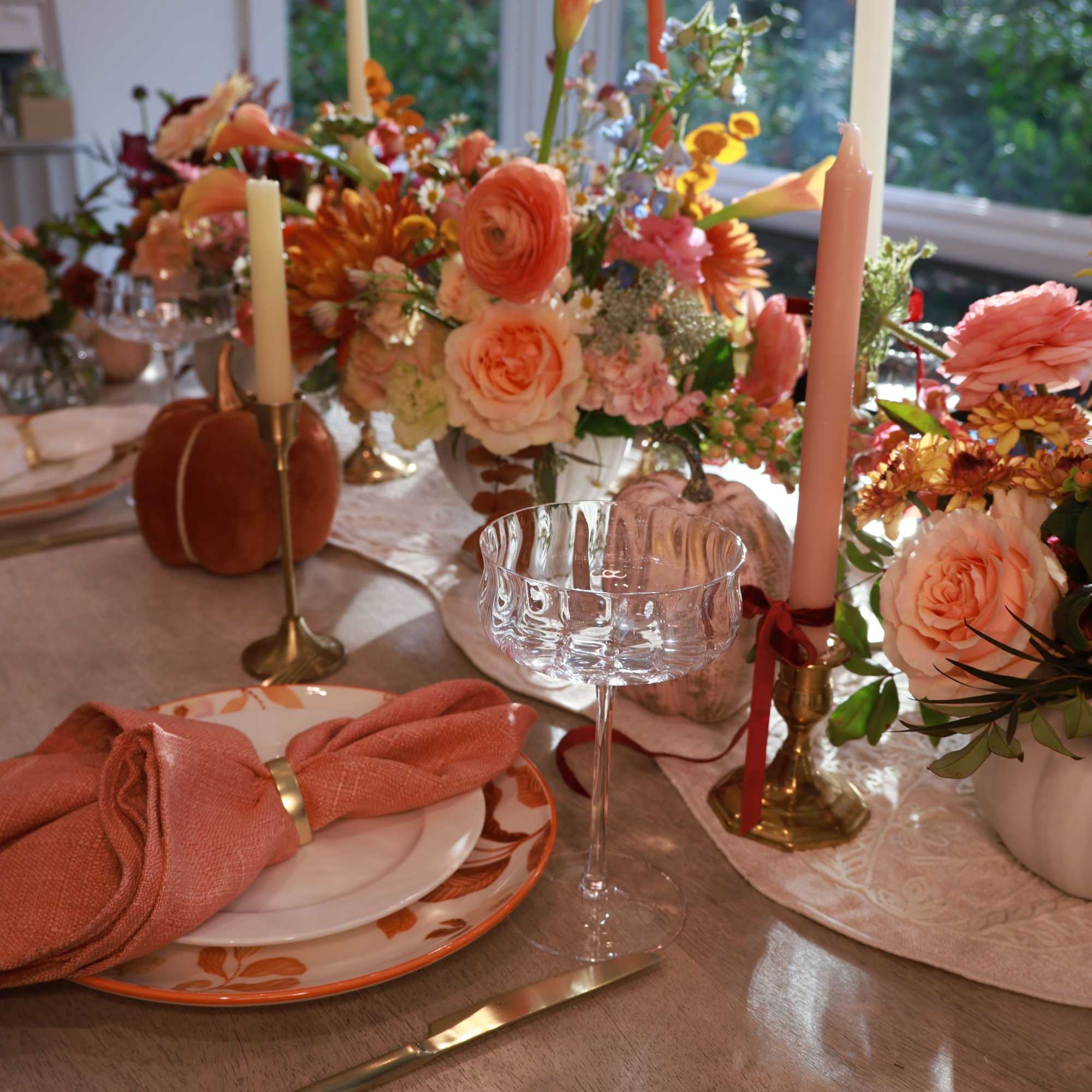 Floral table centerpiece with peach and pink blooms, candles, and pumpkins