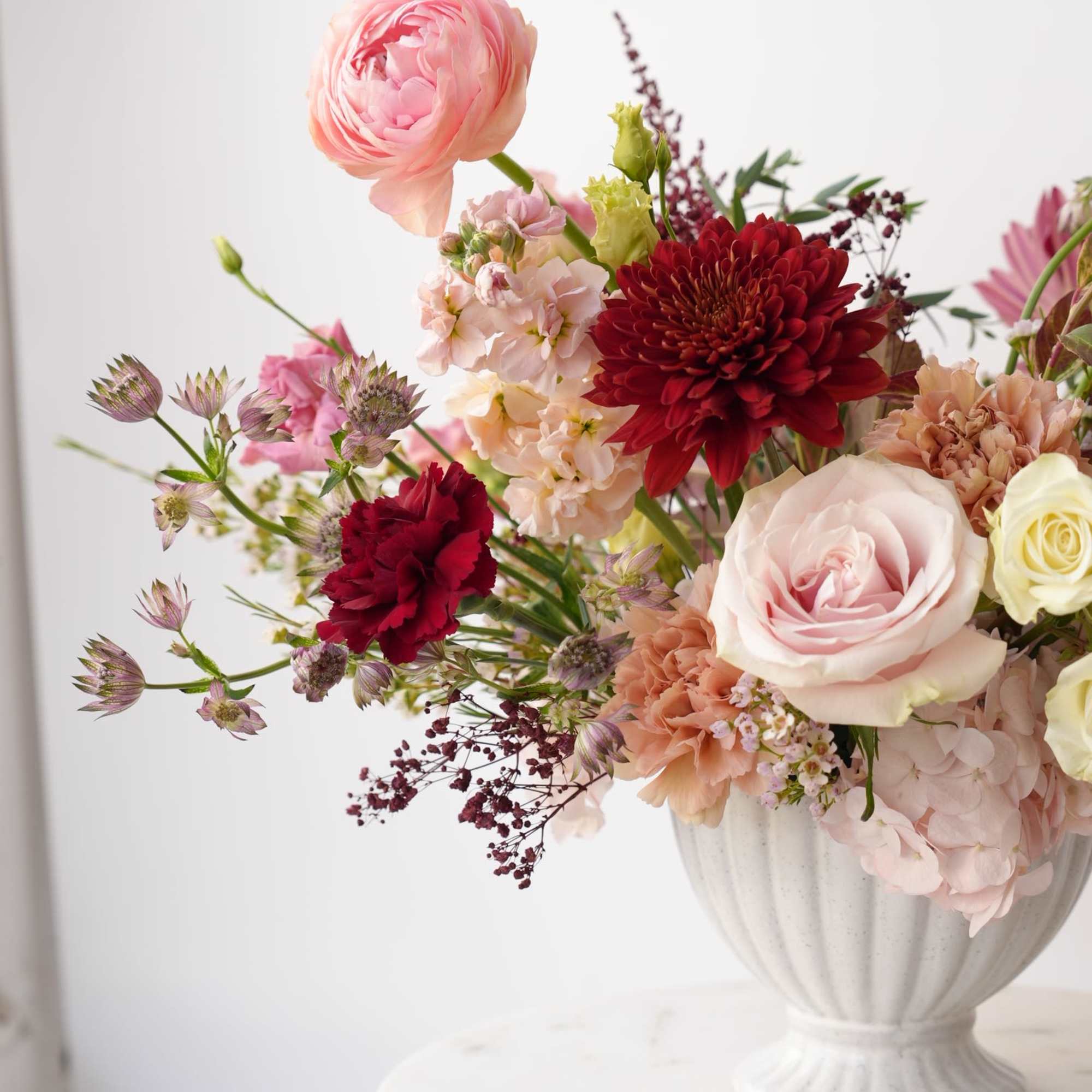 Mixed pink and red flowers arranged in a white vase