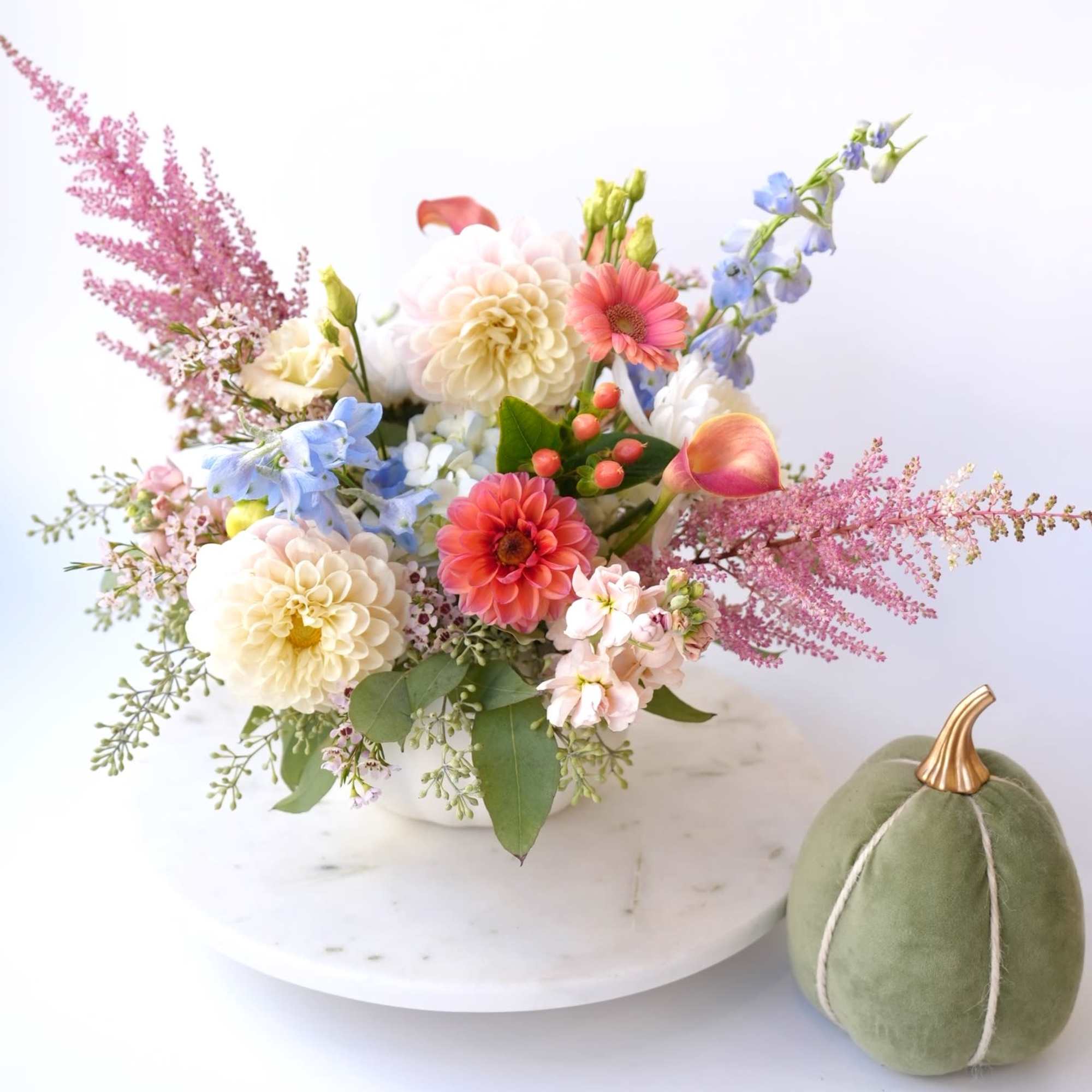 Mixed pastel flower arrangement in a white bowl with a green velvet pumpkin