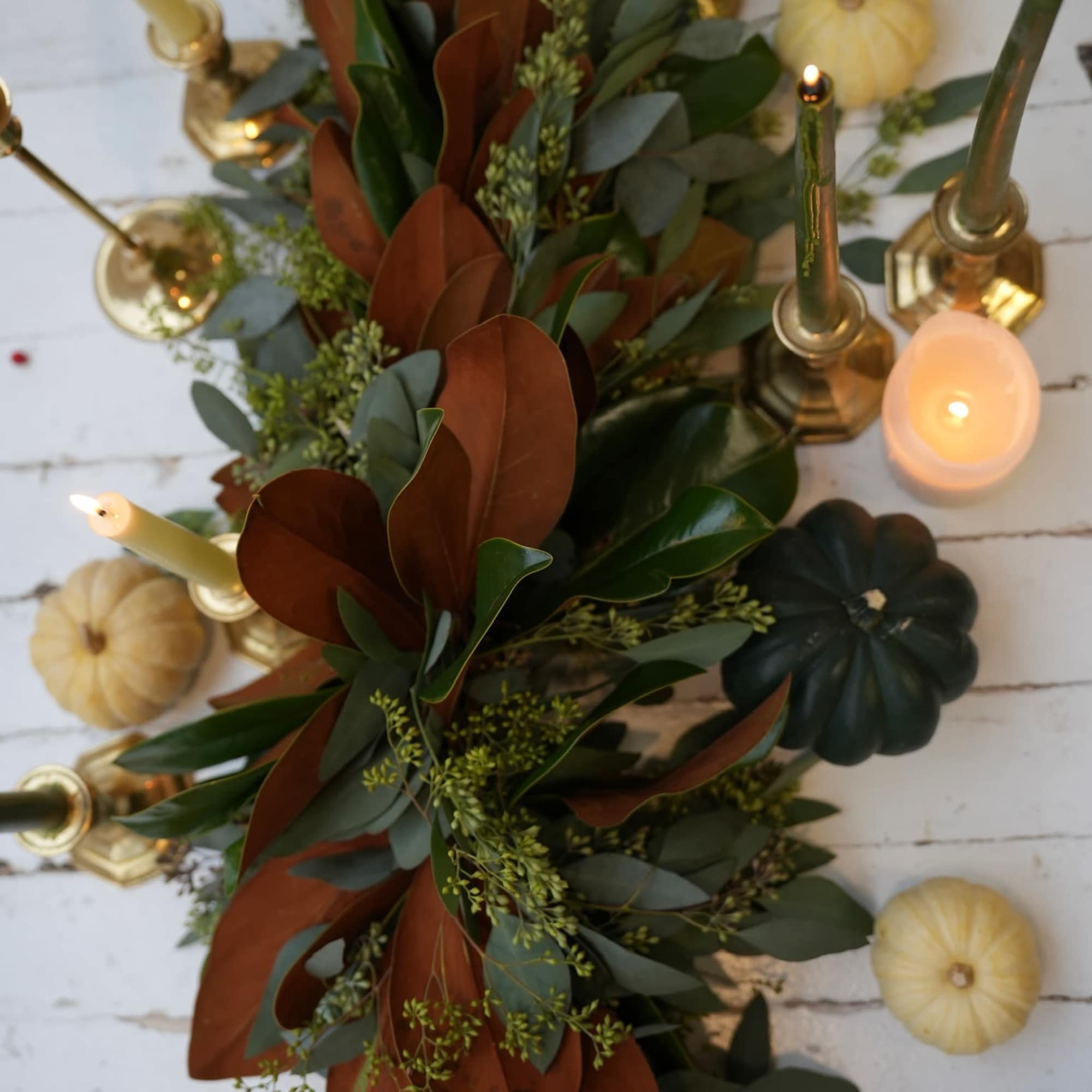 Long greenery garland with candles and small pumpkins on a white table