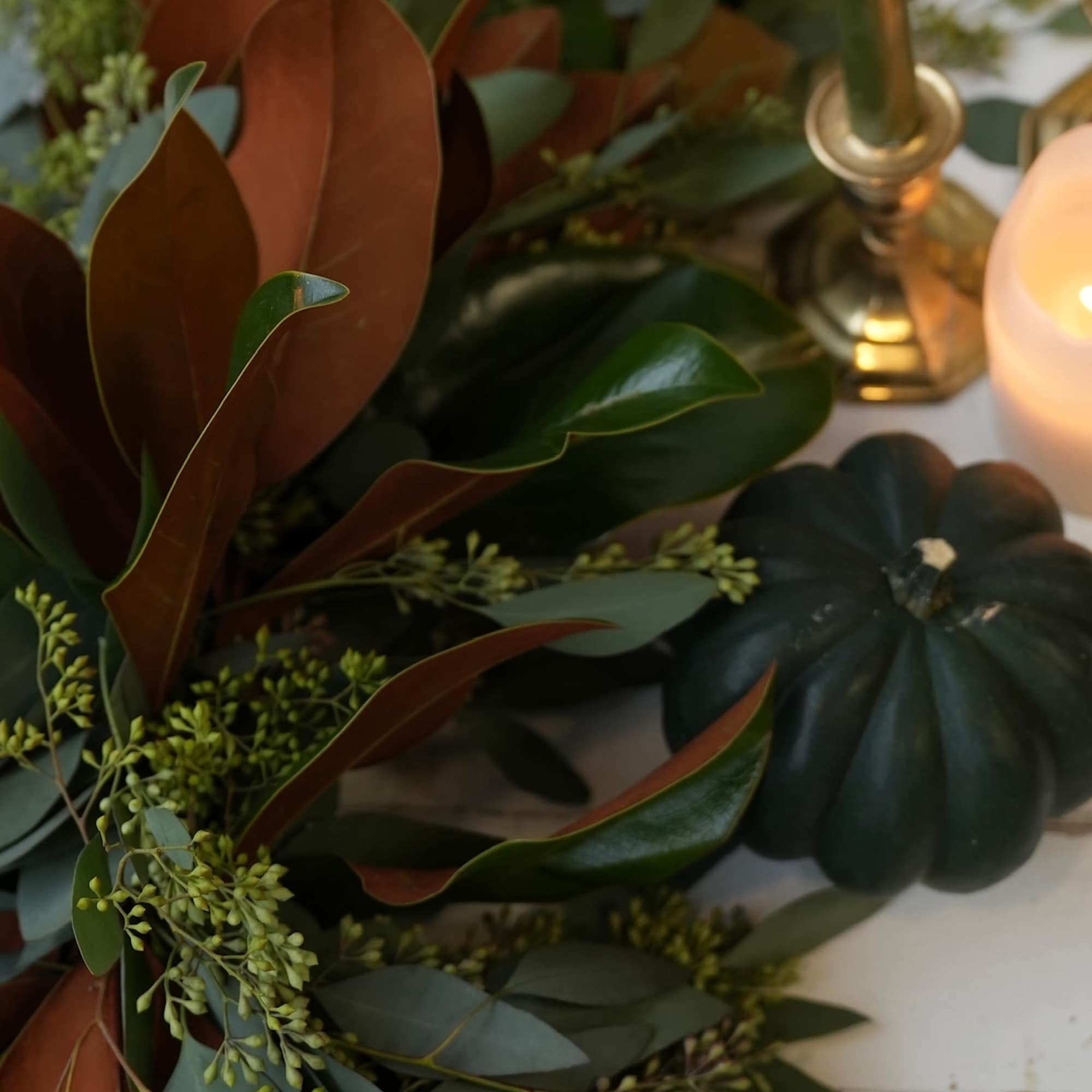 Autumn garland with magnolia leaves, candles, and small pumpkins on a white table