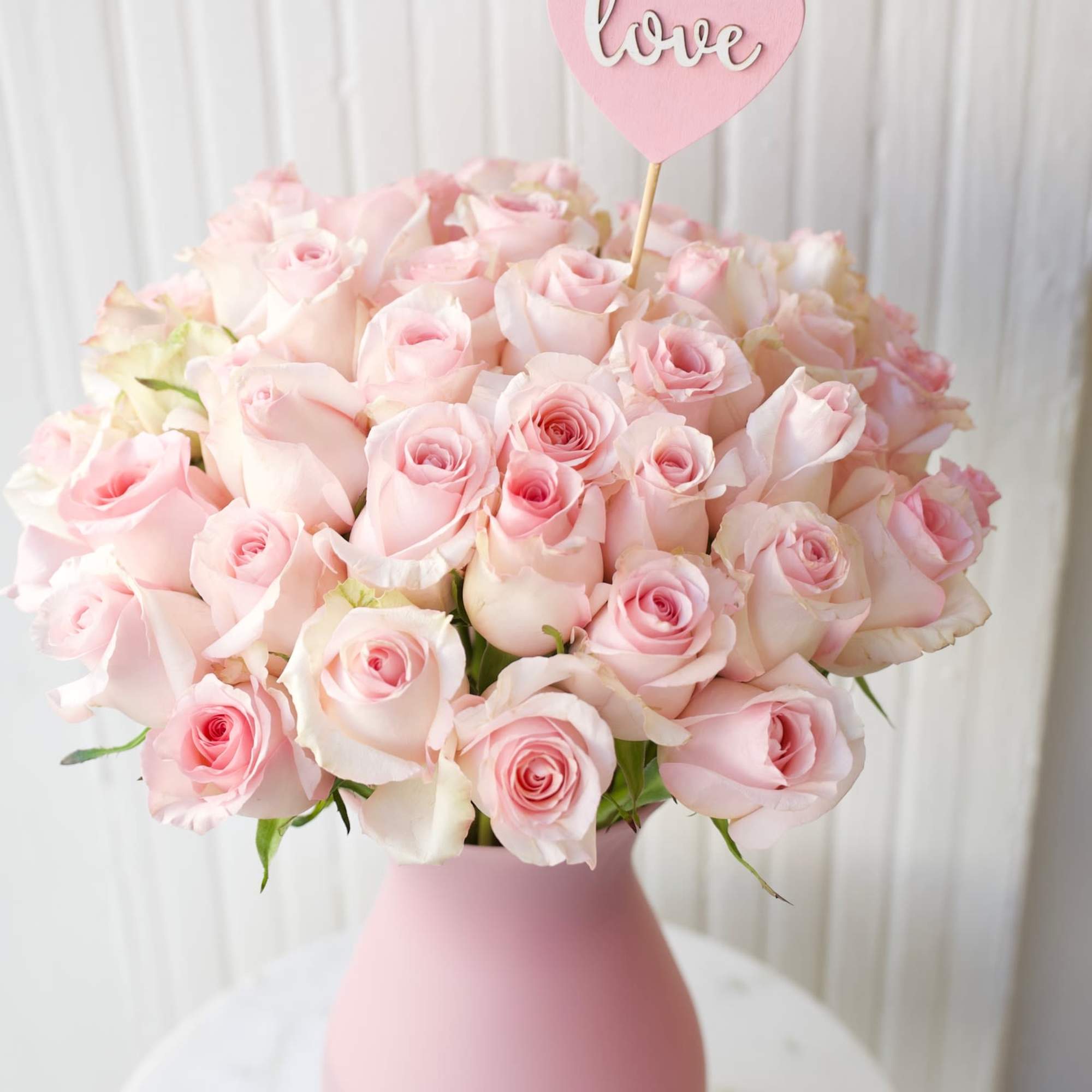 Pink rose bouquet in a matte pink vase with a heart-shaped love pick