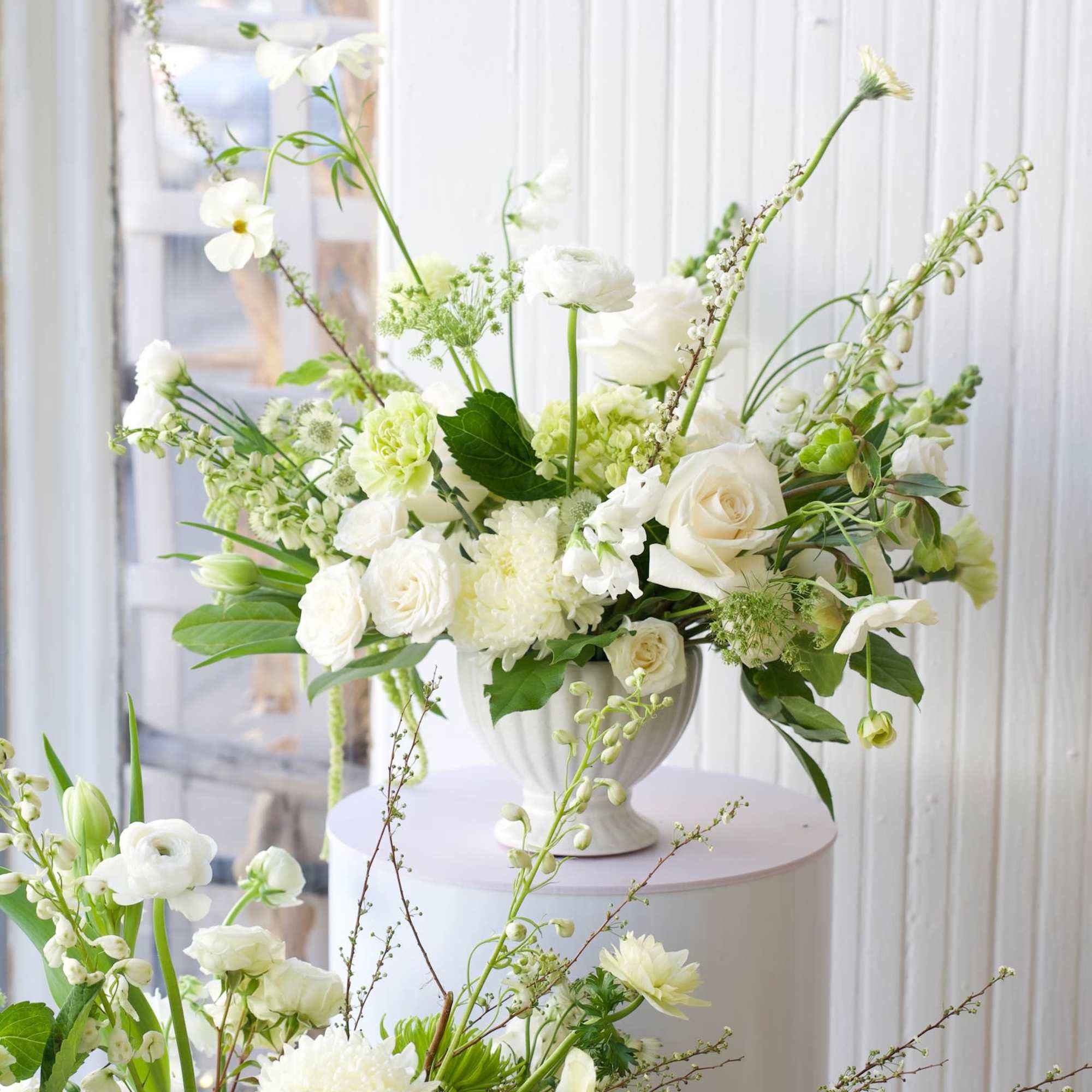 White floral arrangement in a silver urn with roses and tall stems